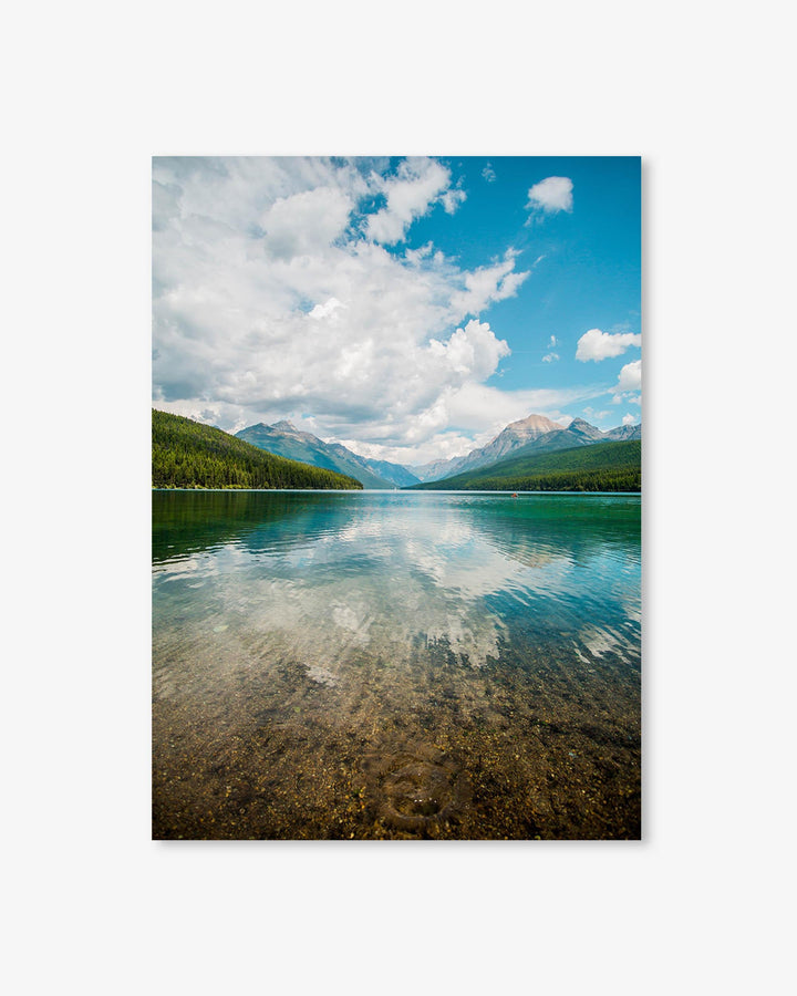 Clear lake with mountains and trees under a blue sky with clouds