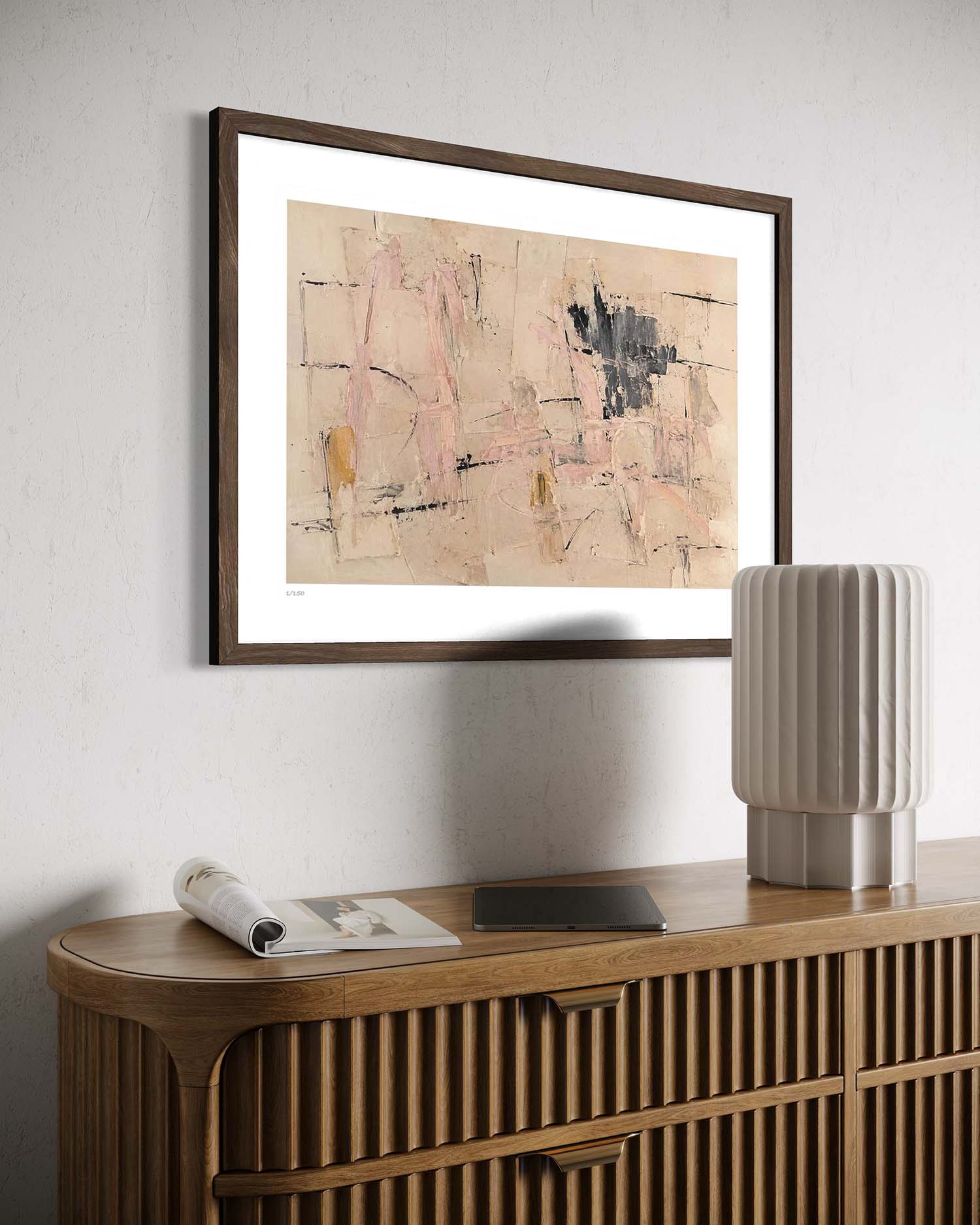 A framed abstract art print with a dark brown frame and white mat, hanging on a light gray textured wall above a wooden credenza with a modern ribbed lamp.