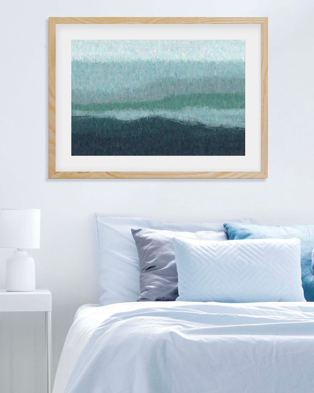 Framed abstract art above a bed with white bedding and blue pillows.