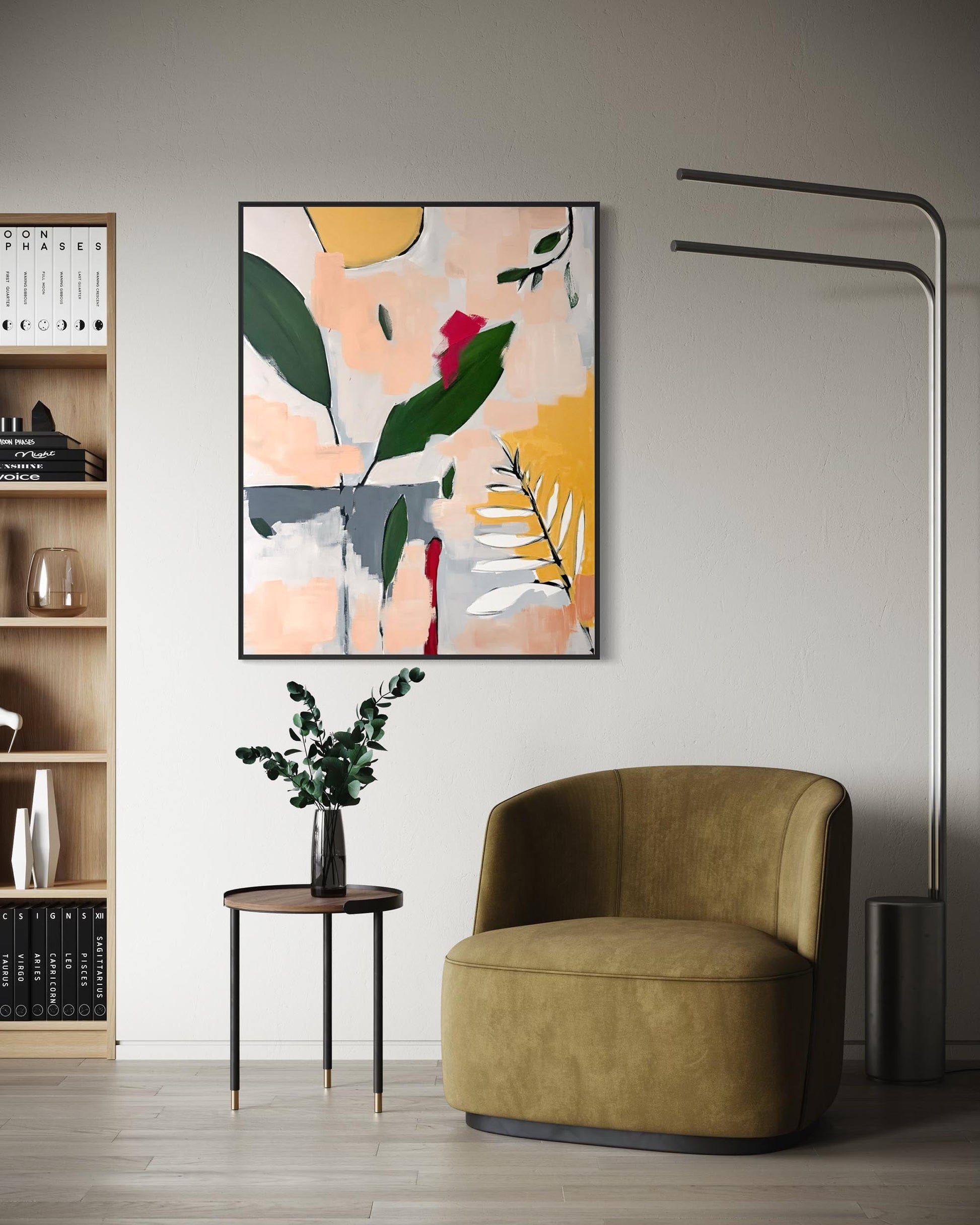 An abstract botanical wall art print with green leaves, yellow and pink shapes, and gray accents, hanging on a light gray wall above a mustard green armchair and a small side table with a vase of greenery.