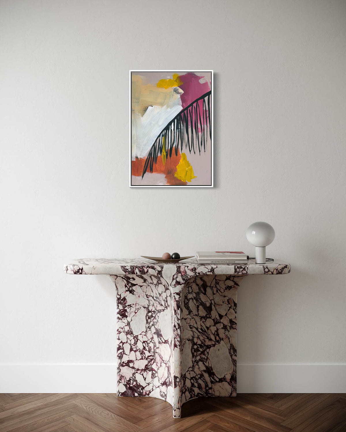 An abstract framed wall art print hangs on a white wall above a sculptural marble console table with a white spherical lamp on a wood floor.