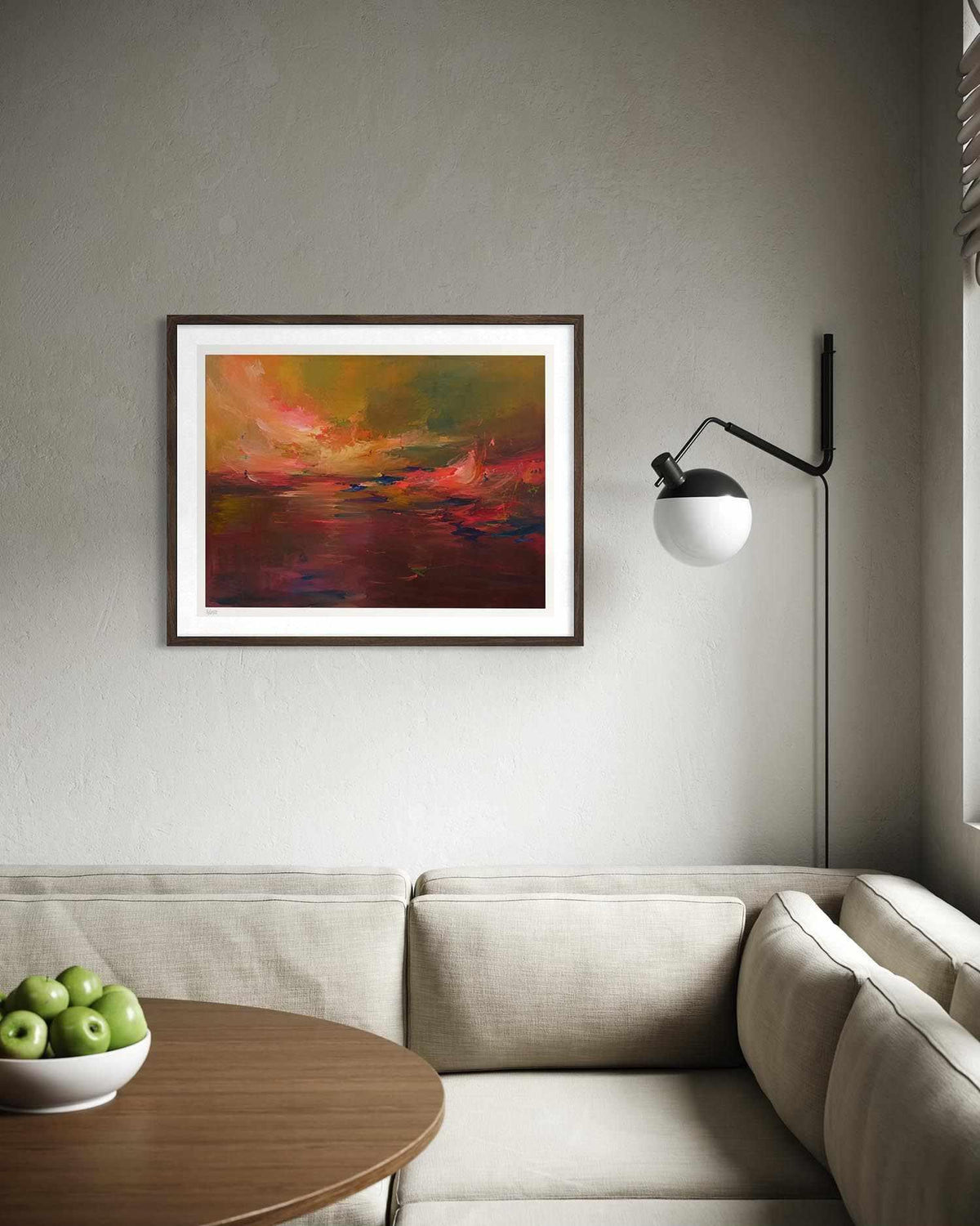 A framed abstract landscape painting with warm red, orange, yellow, and green tones hangs on a light gray wall above a beige sofa in a modern living room setting.