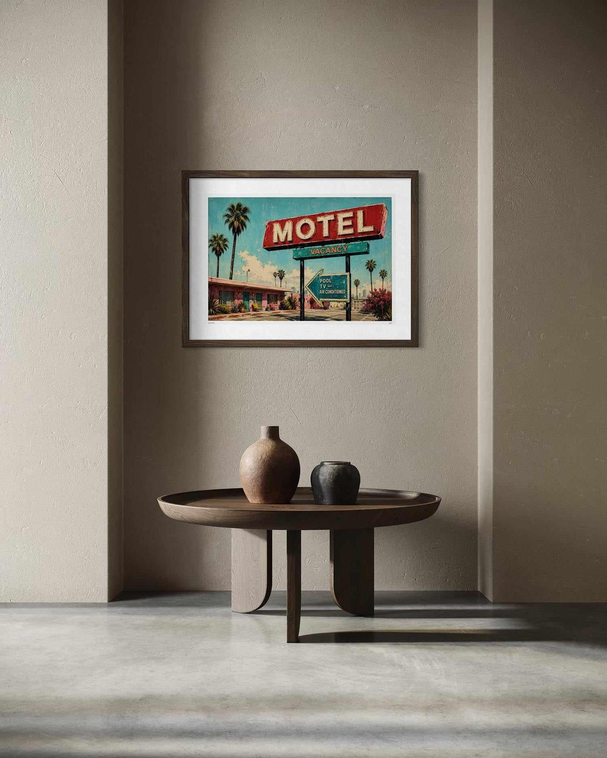 A framed art print depicting a retro motel sign and palm trees, displayed on a beige wall above a round wooden table with decorative vases.