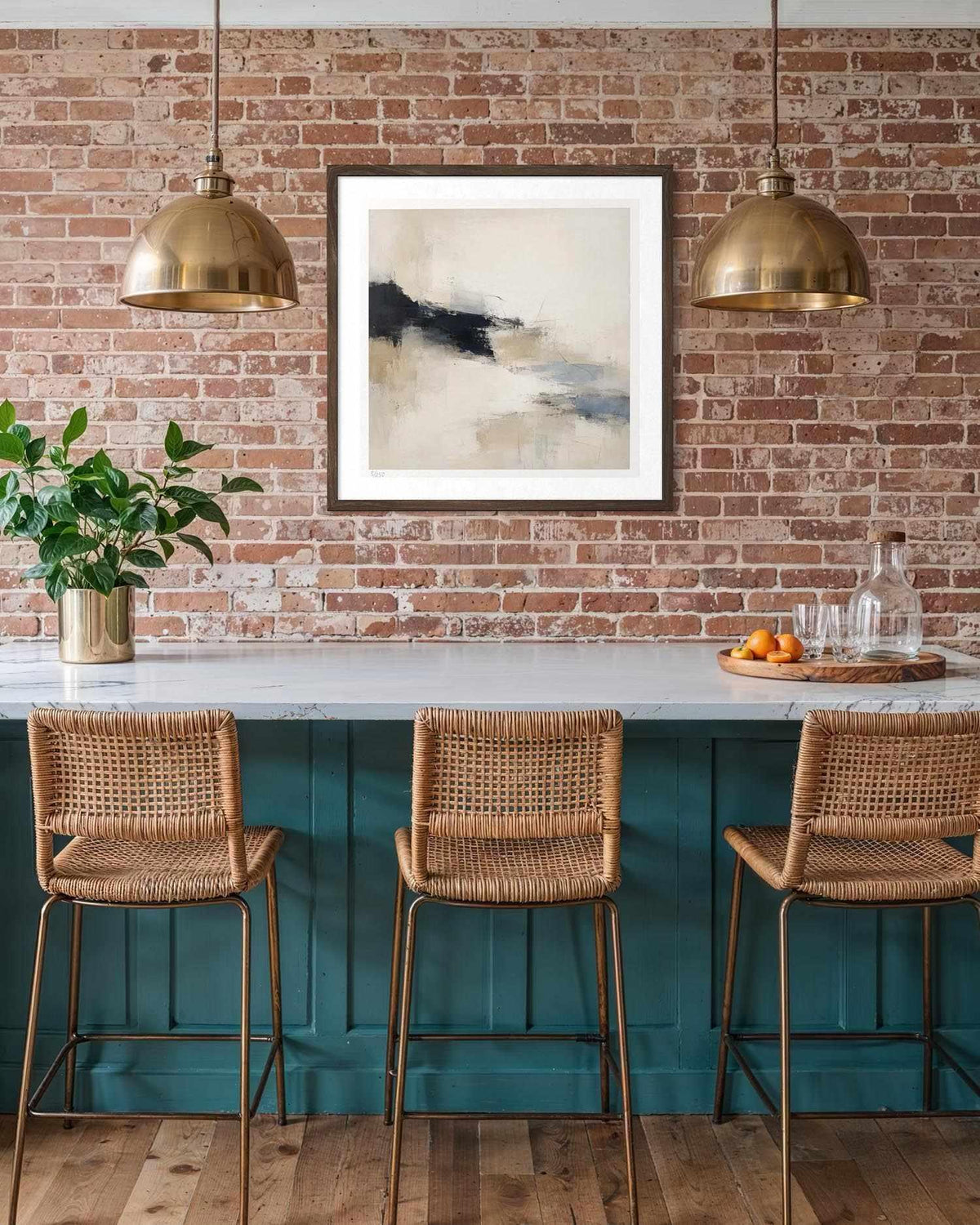 A framed abstract landscape art print with black, white, and gray tones hangs on a brick wall above a teal bar counter with three woven wicker bar stools and brass pendant lights.