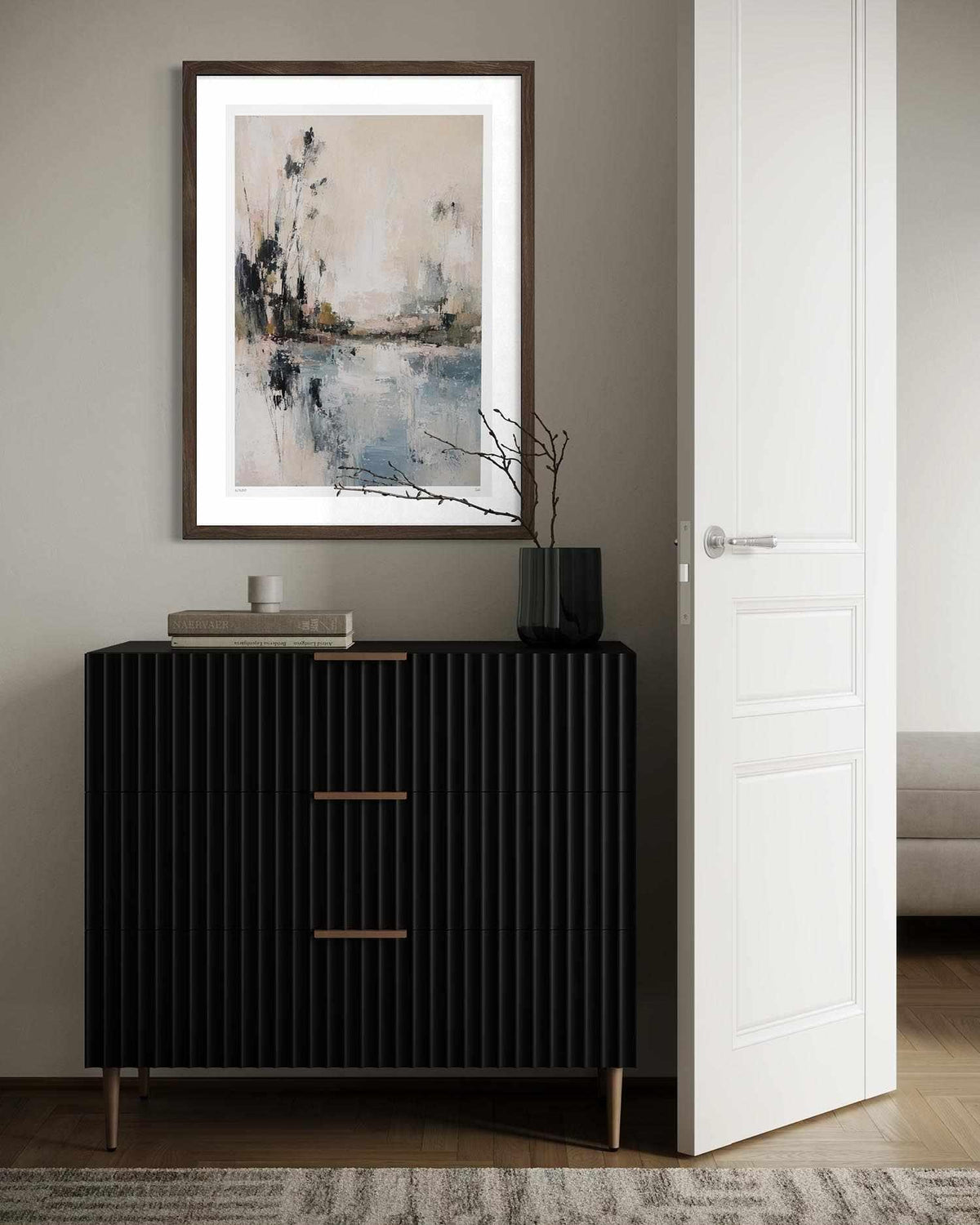 A framed abstract landscape art print with a white mat and dark wood frame hangs on a gray wall above a black ribbed console cabinet in a modern interior setting.
