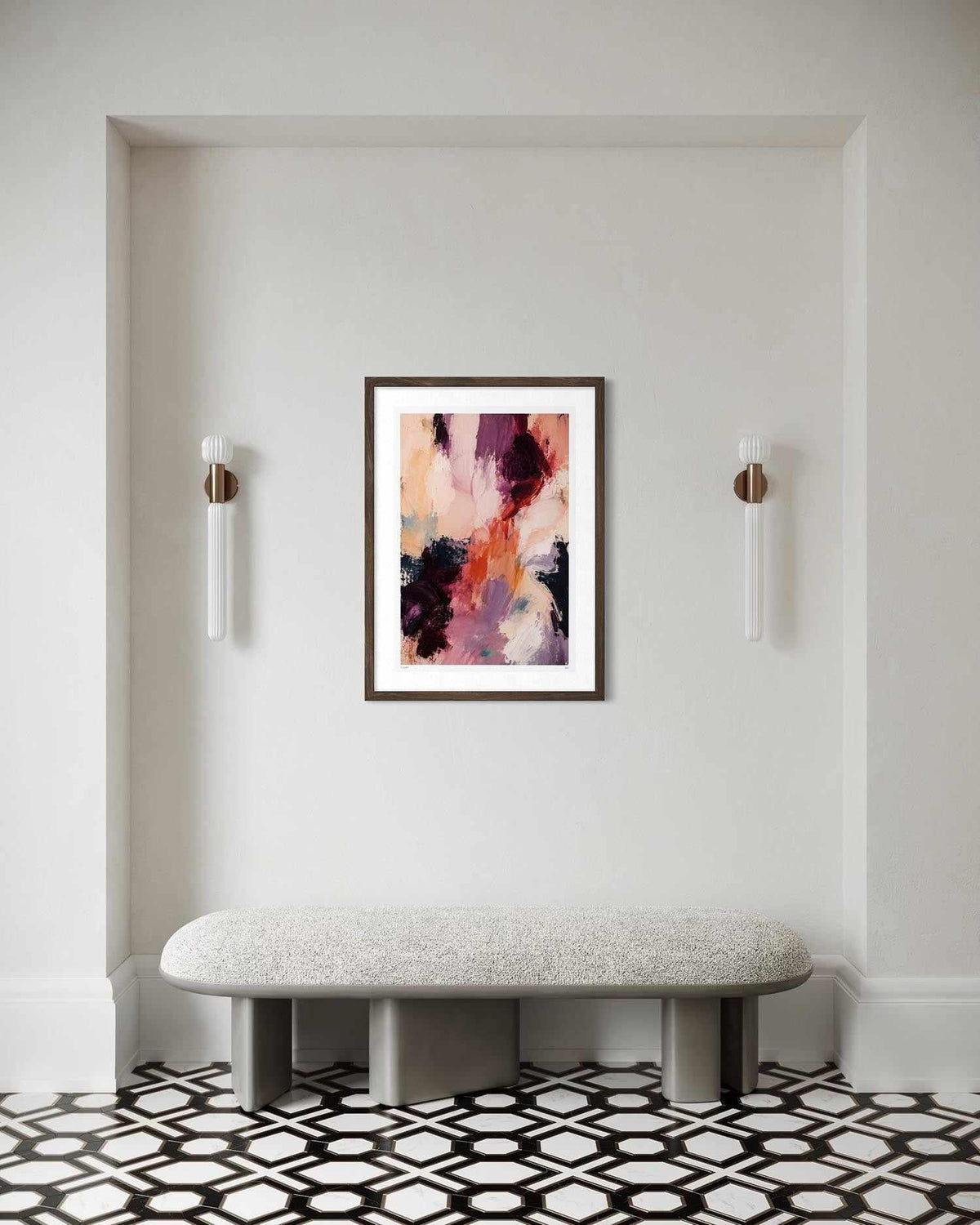 A framed abstract painting with pink, purple, orange, and black brushstrokes hangs on a white wall above a light gray bench in a modern interior setting with black and white geometric tile flooring.