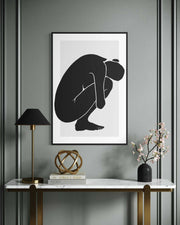 Framed abstract art of a black silhouette on a gray wall above a marble console table.