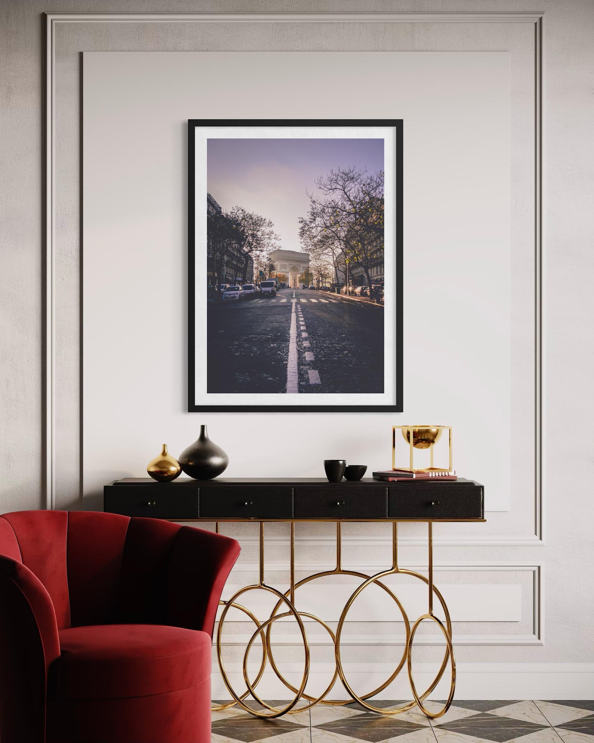 Framed artwork on a wall above a console table with decorative items, featuring a red armchair and gold circular console.