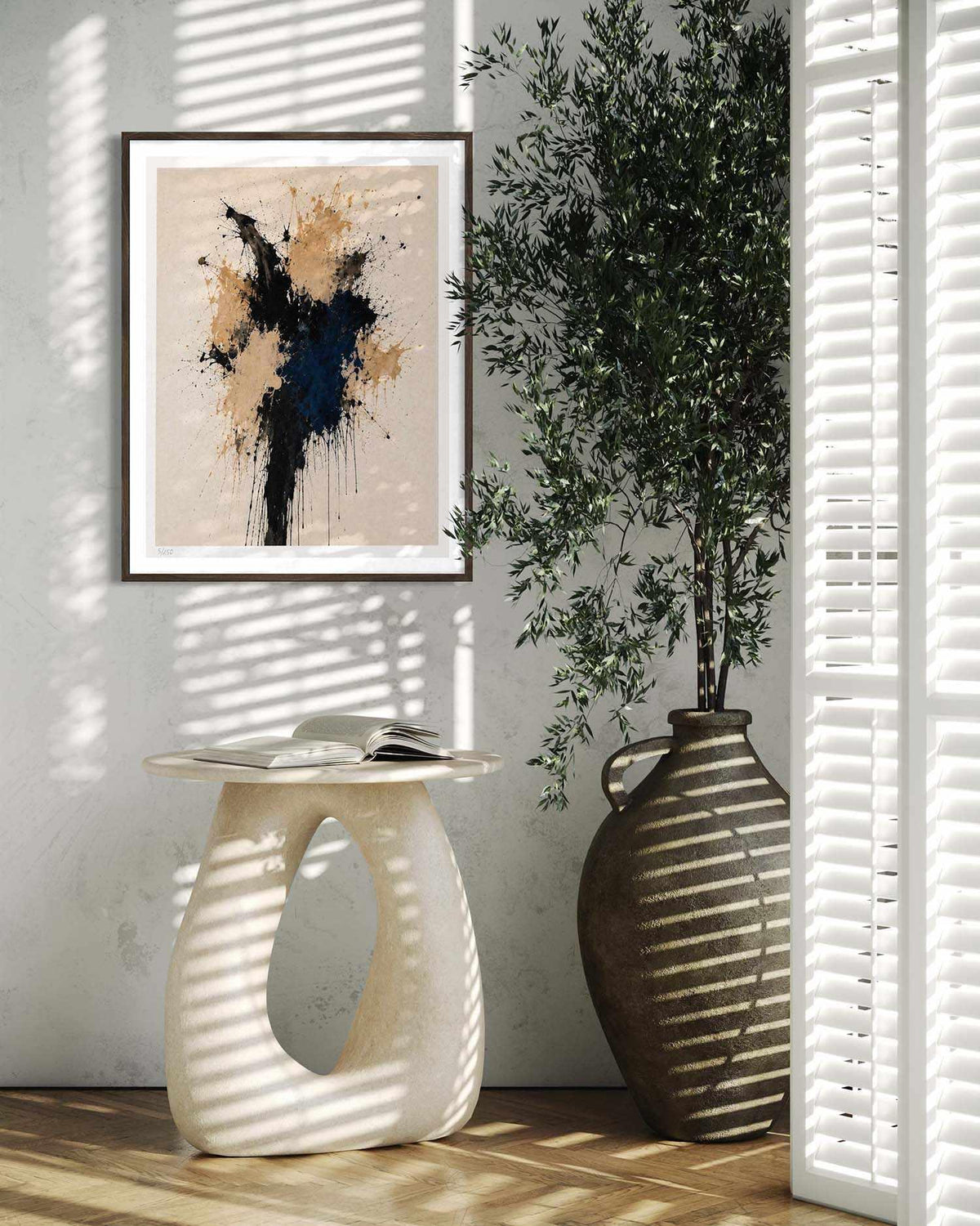 A framed abstract art print hangs on a light gray wall in a styled interior scene with a sculptural white side table, a large brown ceramic vase, and a tall green plant, all cast in soft window shadow.