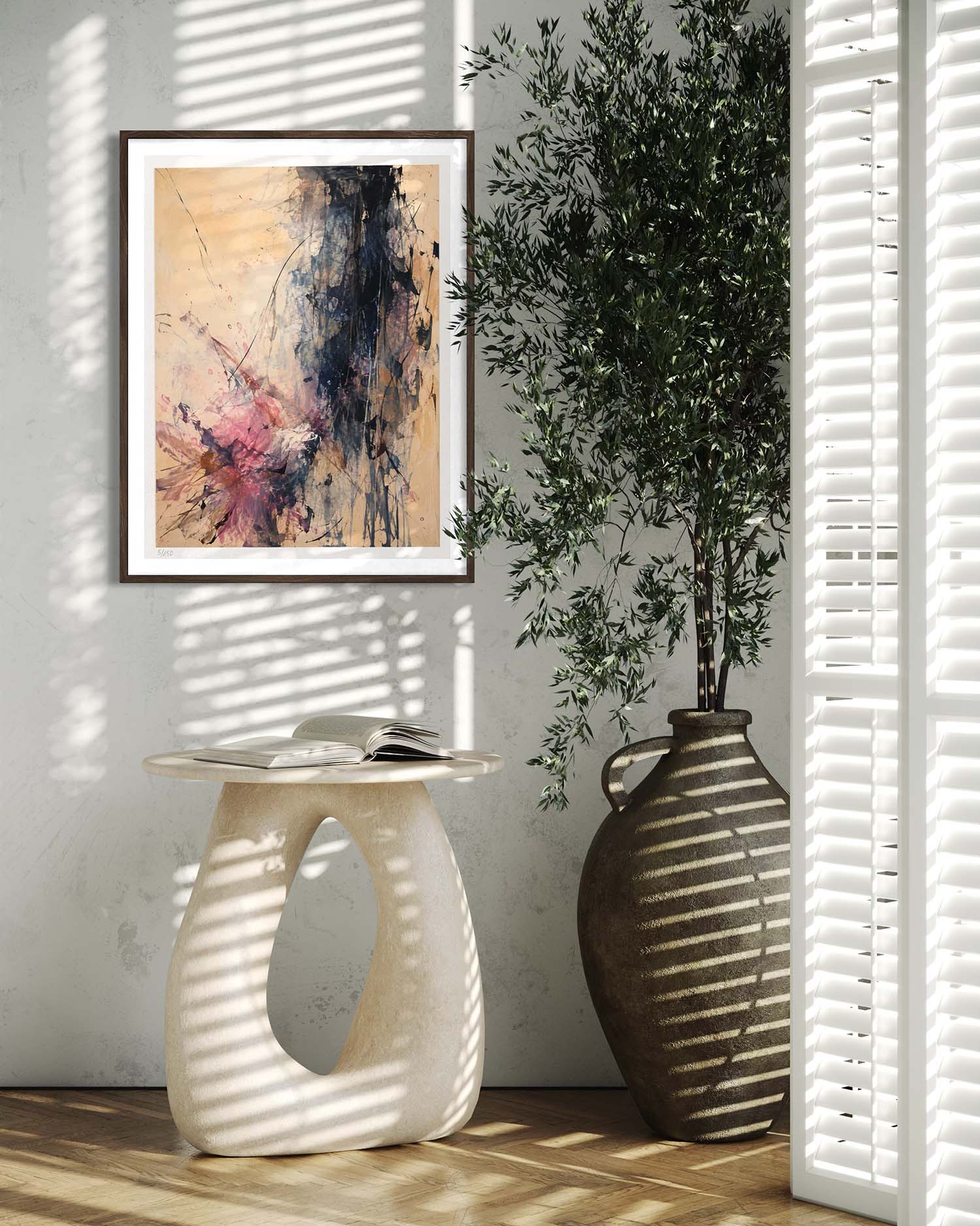 A framed abstract art print hangs on a light gray wall in a styled interior scene with a sculptural side table, a large vase with a tree, and window blinds casting striped shadows.
