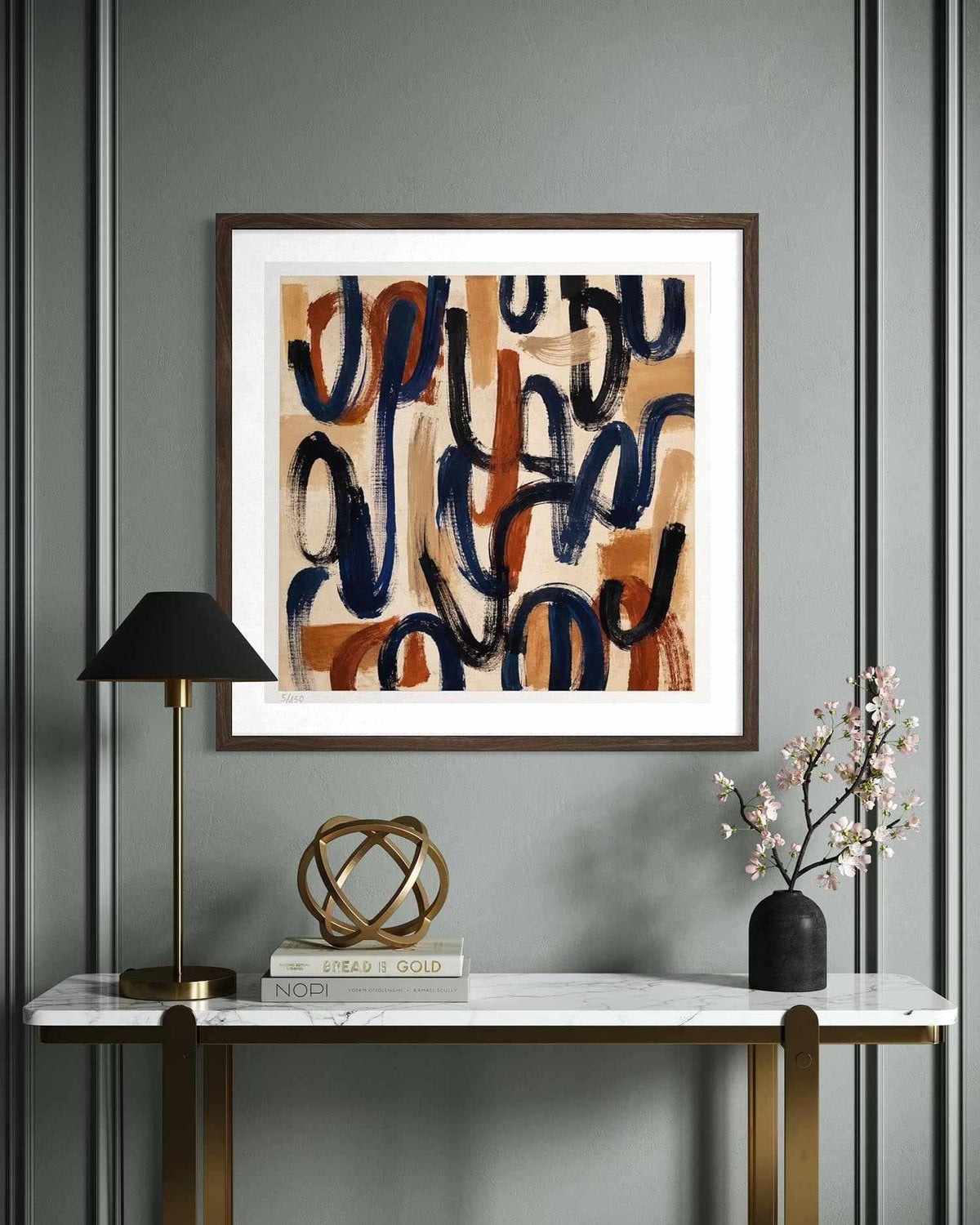 Framed abstract wall art hanging above a console table in a styled interior. The artwork features flowing, organic brushstrokes in navy blue, terracotta orange, beige, and brown on a white mat, set in a dark wood frame.