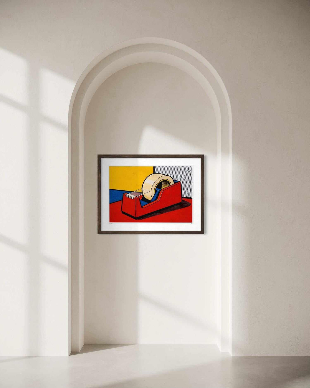 A framed pop art print of a tape dispenser is displayed on a beige wall within a white arched niche. The artwork features bold blocks of yellow, blue, red, and gray with a white roll of tape, enclosed in a thin black frame.