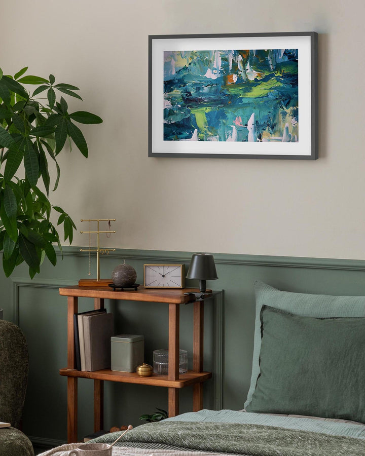 Framed abstract painting on a wall above a wooden shelf in a room with green walls and a plant.
