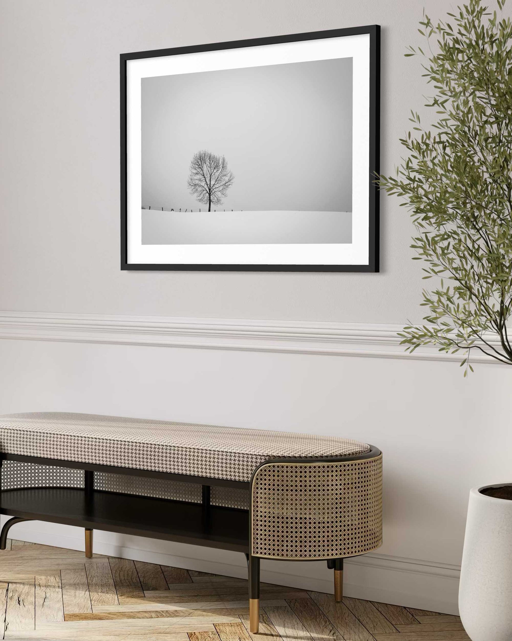 Framed black and white photograph of a tree on a snowy landscape above a modern console table.