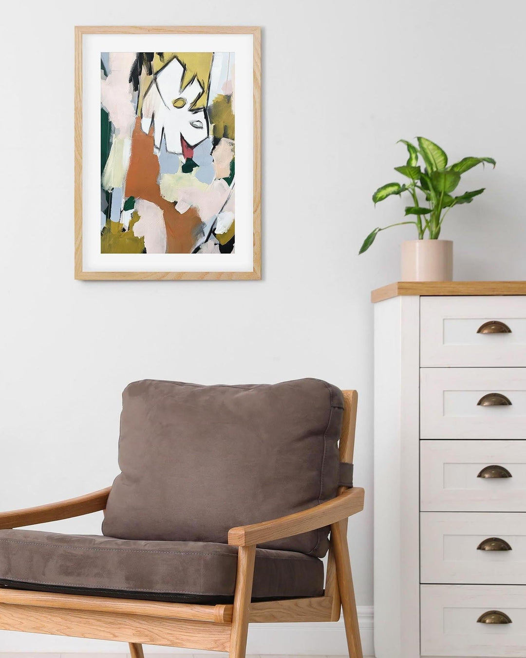 Modern interior with a brown cushioned chair, white dresser, and abstract art on the wall.