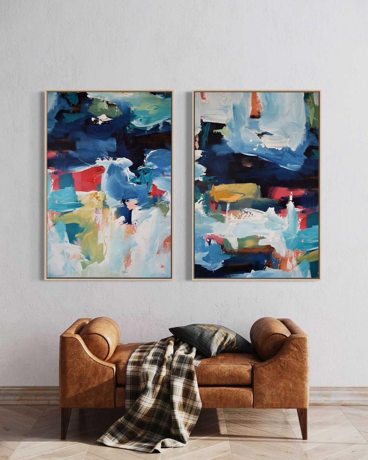 Two abstract paintings on a wall above a brown sofa with a plaid blanket.