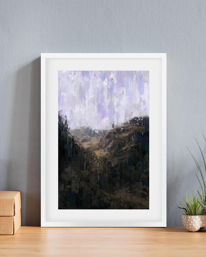 Framed abstract artwork on a wall with a plant and wooden box in the foreground.