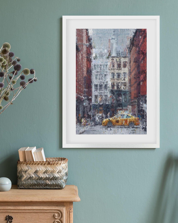 Framed artwork of a snowy city street with a yellow taxi on a teal wall above a wooden cabinet.