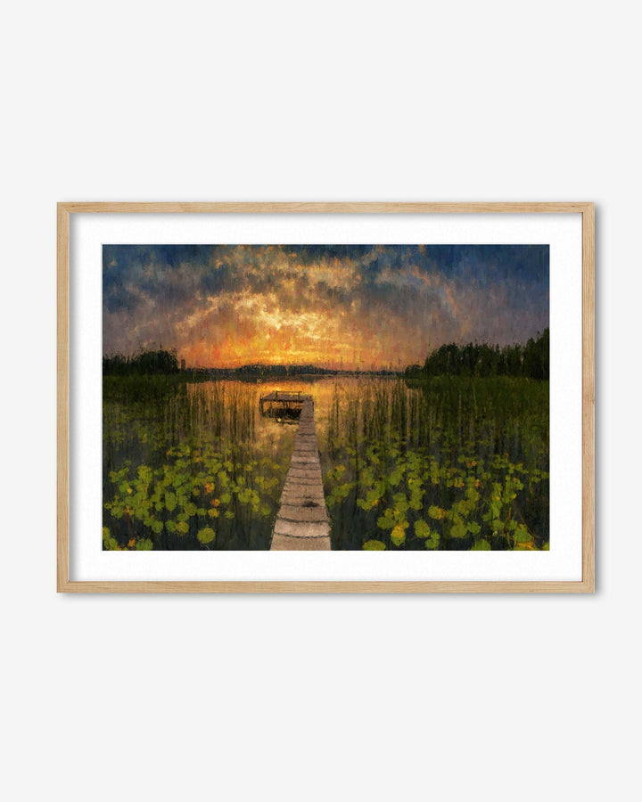 Framed artwork of a sunset over a lake with a dock and floating lily pads.