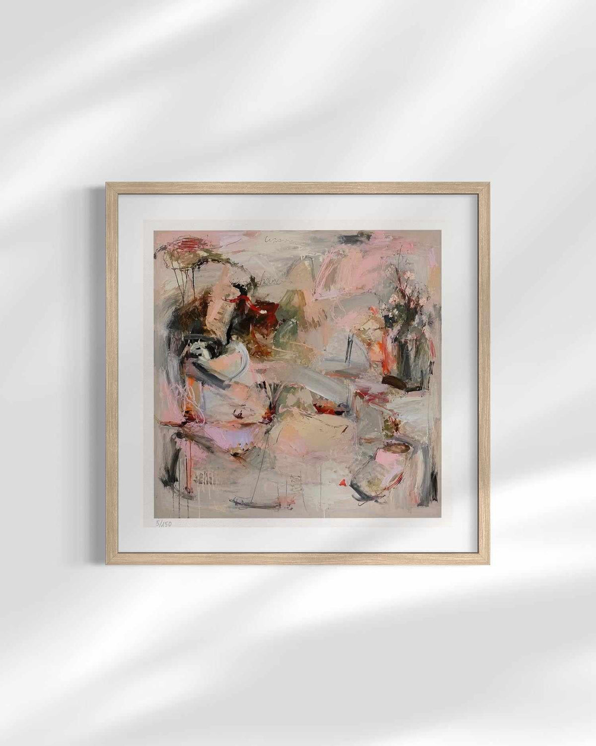 A framed abstract painting featuring soft pink, beige, gray, and black brushstrokes, presented in a light wood frame with a white mat against a white wall with soft leaf shadows.