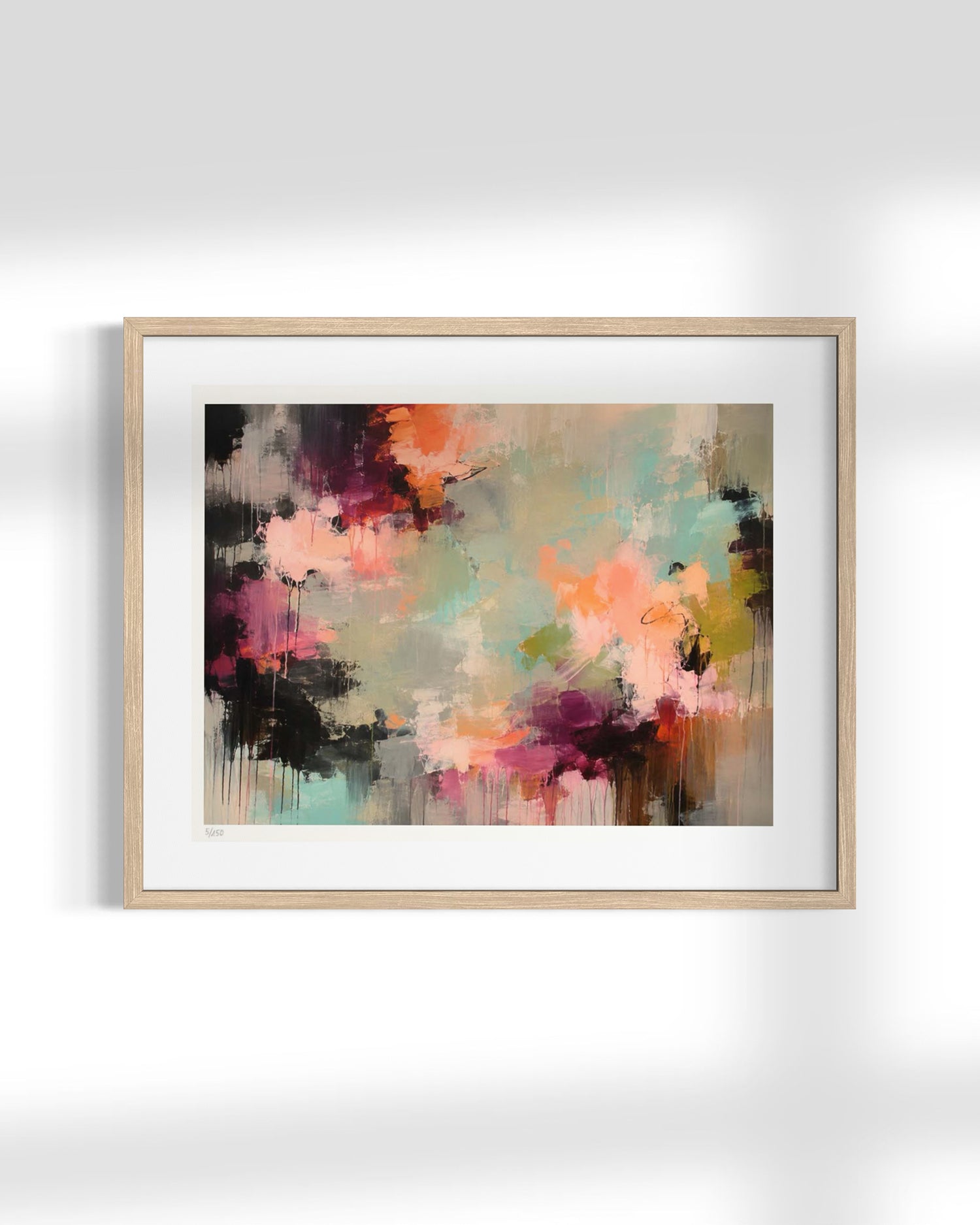 Framed abstract wall art with a light wood frame and white mat, featuring a multicolor paint splatter design in pink, orange, teal, purple, black, and beige tones, displayed against a light gray wall.