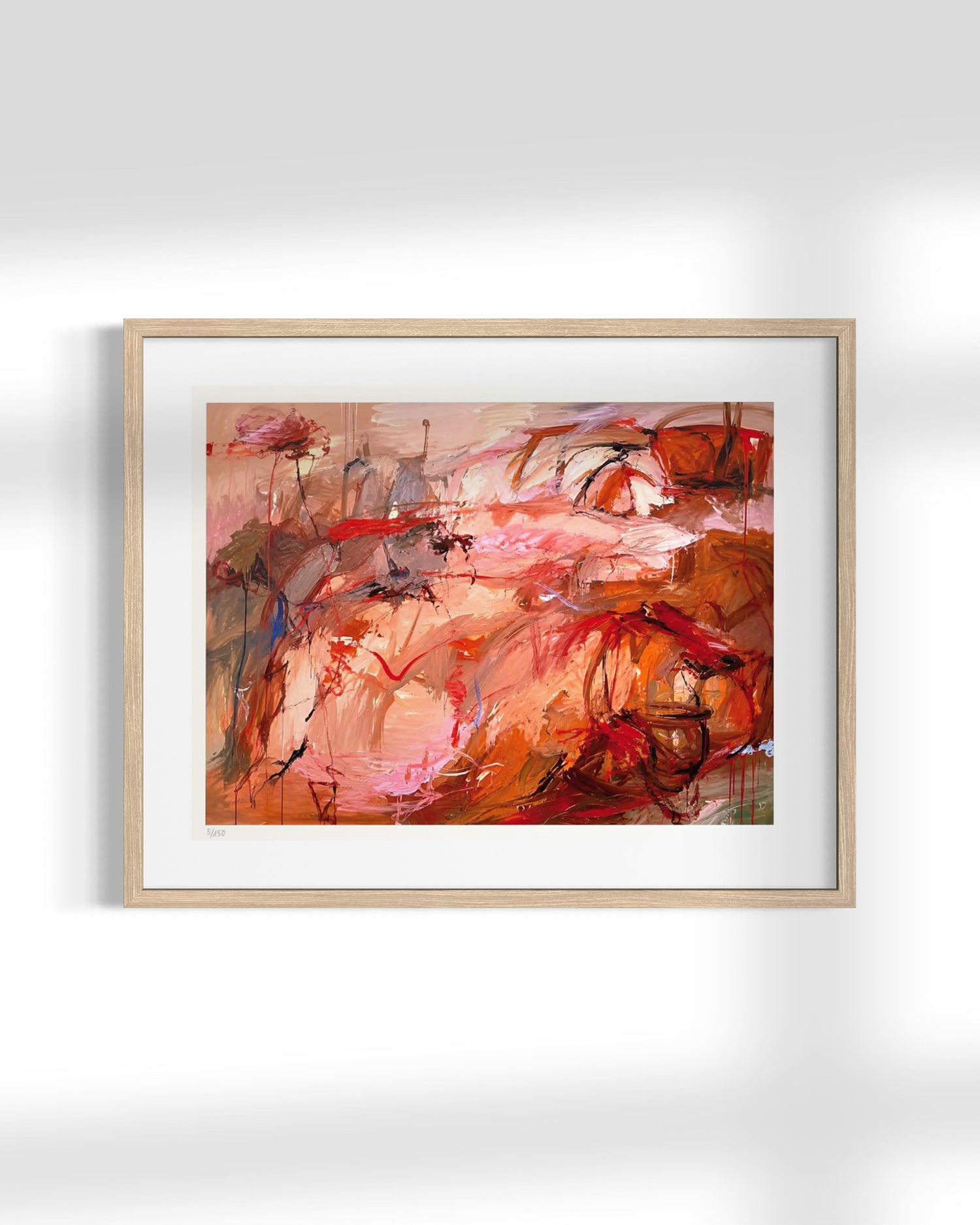 An abstract framed painting featuring expressive brushstrokes in warm tones of red, orange, pink, and brown, presented in a light natural wood frame with a white mat against a clean white wall.