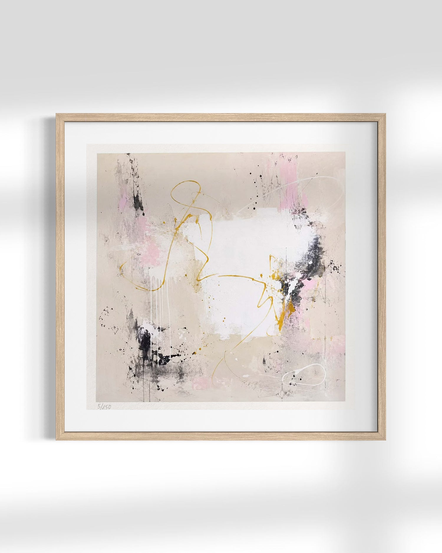 A framed abstract art print featuring a minimalist composition with pink, black, and gold brushstrokes on a warm beige background, housed in a light natural wood frame with a white mat.