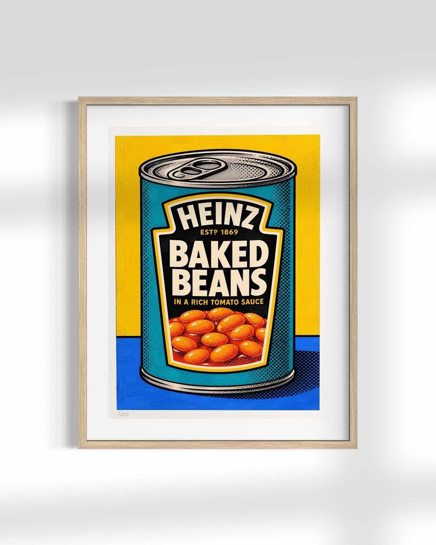 A framed pop-art print of a vintage Heinz Baked Beans can, featuring a yellow and blue background with illustrated beans, set in a light wood frame against a white wall.