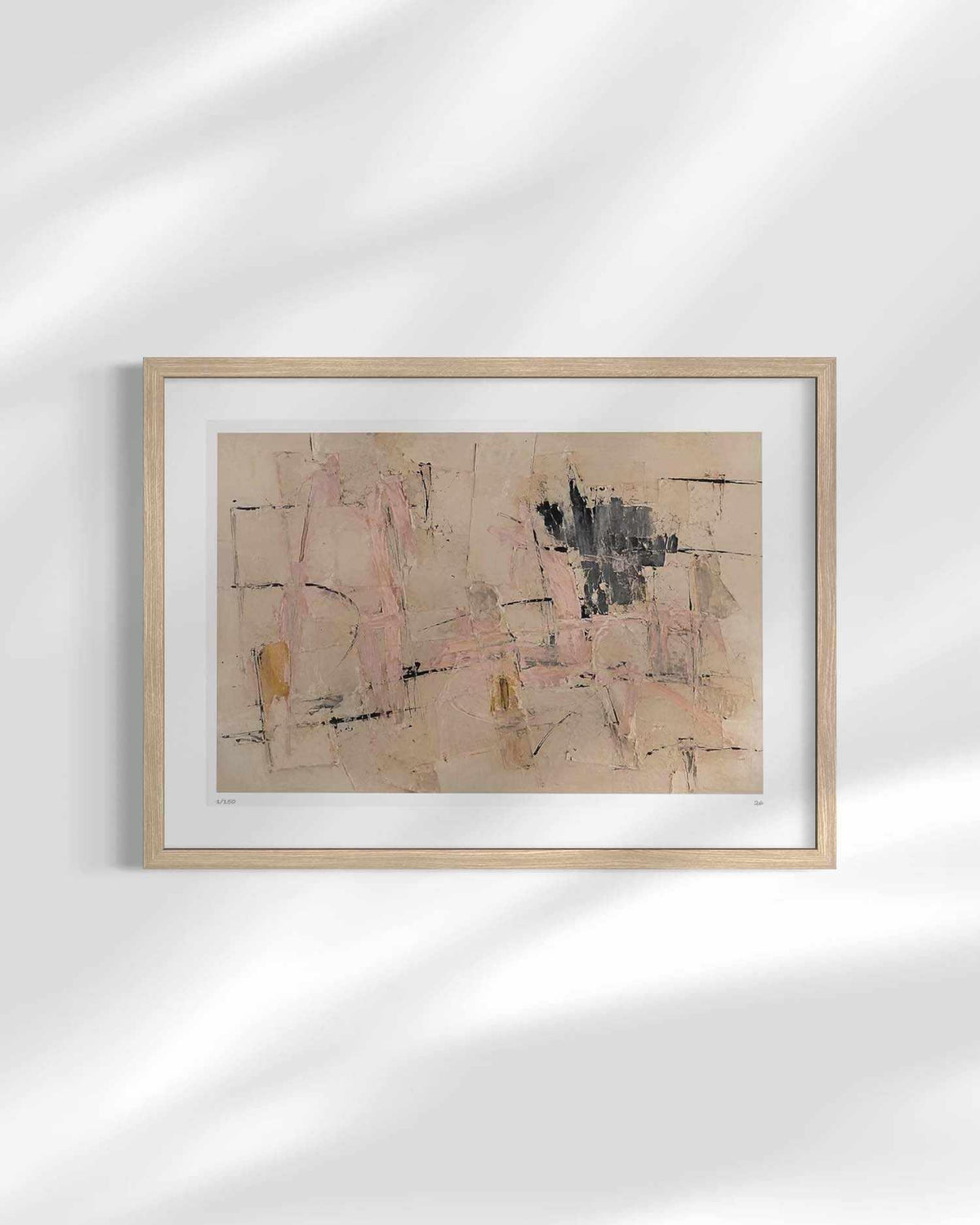 A framed abstract art print featuring beige, pink, black, and brown tones, displayed on a white wall with soft leaf shadows.