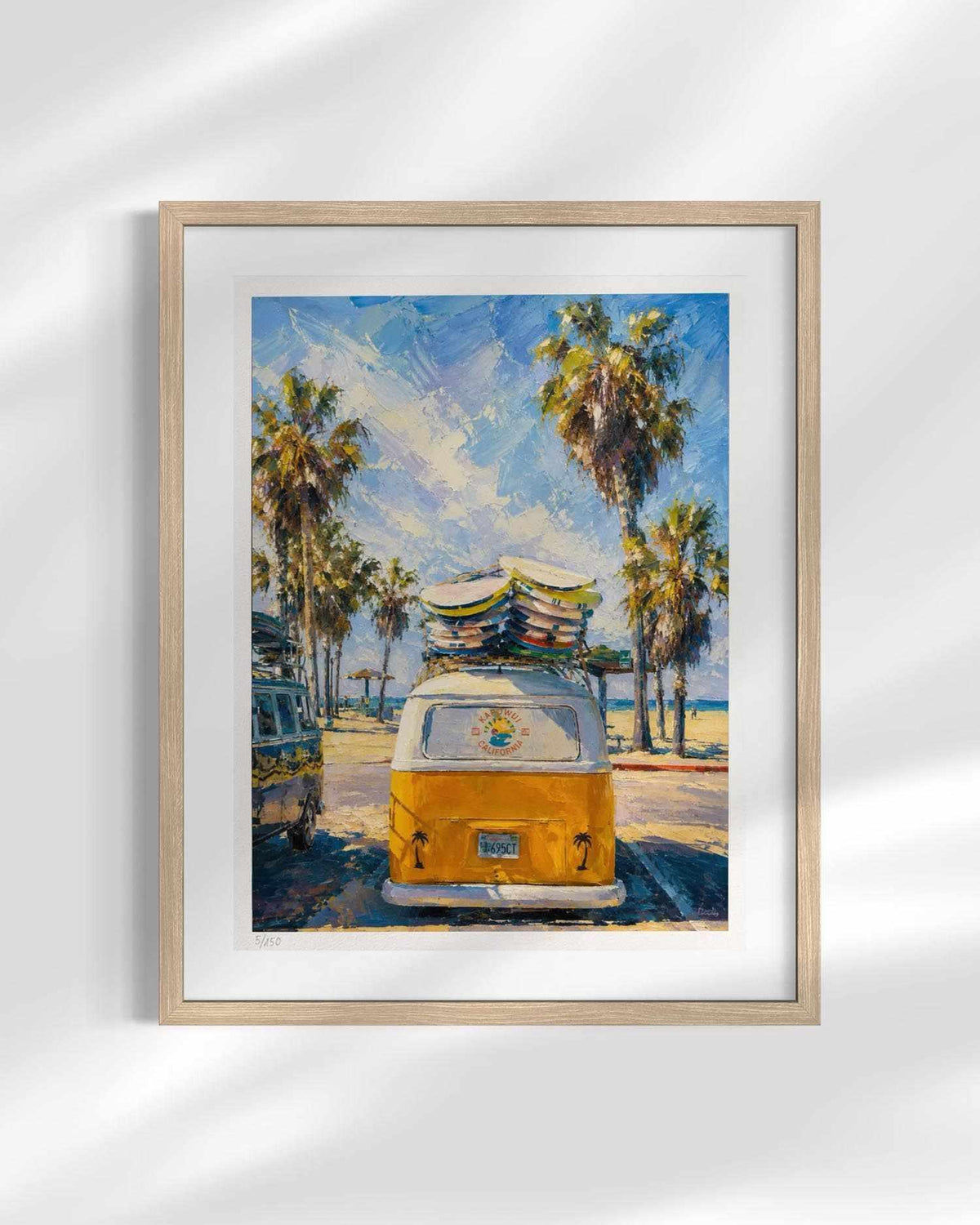 A framed art print featuring an impressionistic painting of a yellow vintage camper van with surfboards on its roof, parked among palm trees under a blue sky. The print is displayed in a light wood frame with a white mat against a white background with soft shadow overlays.