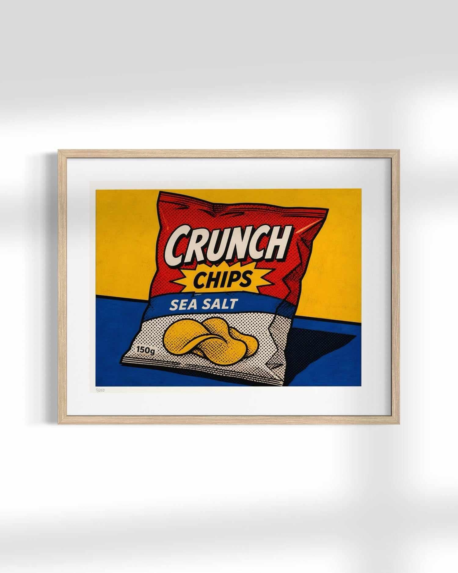 A framed pop-art style print of a Crunch Chips Sea Salt bag, shown hanging on a light gray wall. The artwork features a red bag with yellow and blue sections, with yellow potato chips illustrated on the front.