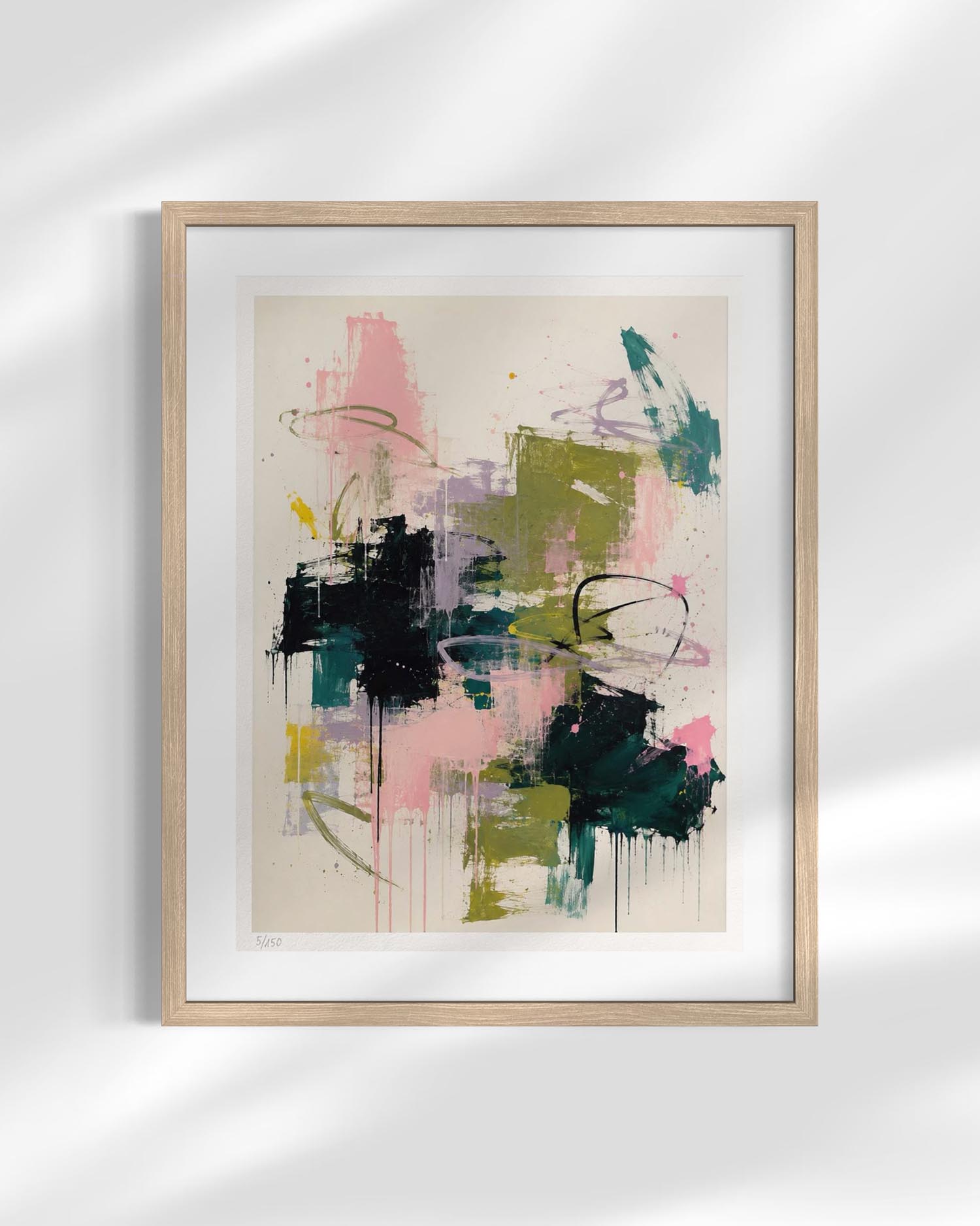 Framed abstract art print featuring expressive brushstrokes in pink, green, black, teal, and purple on a warm beige background, housed in a light natural wood frame with a white mat, shown against a white wall with soft shadow overlays.