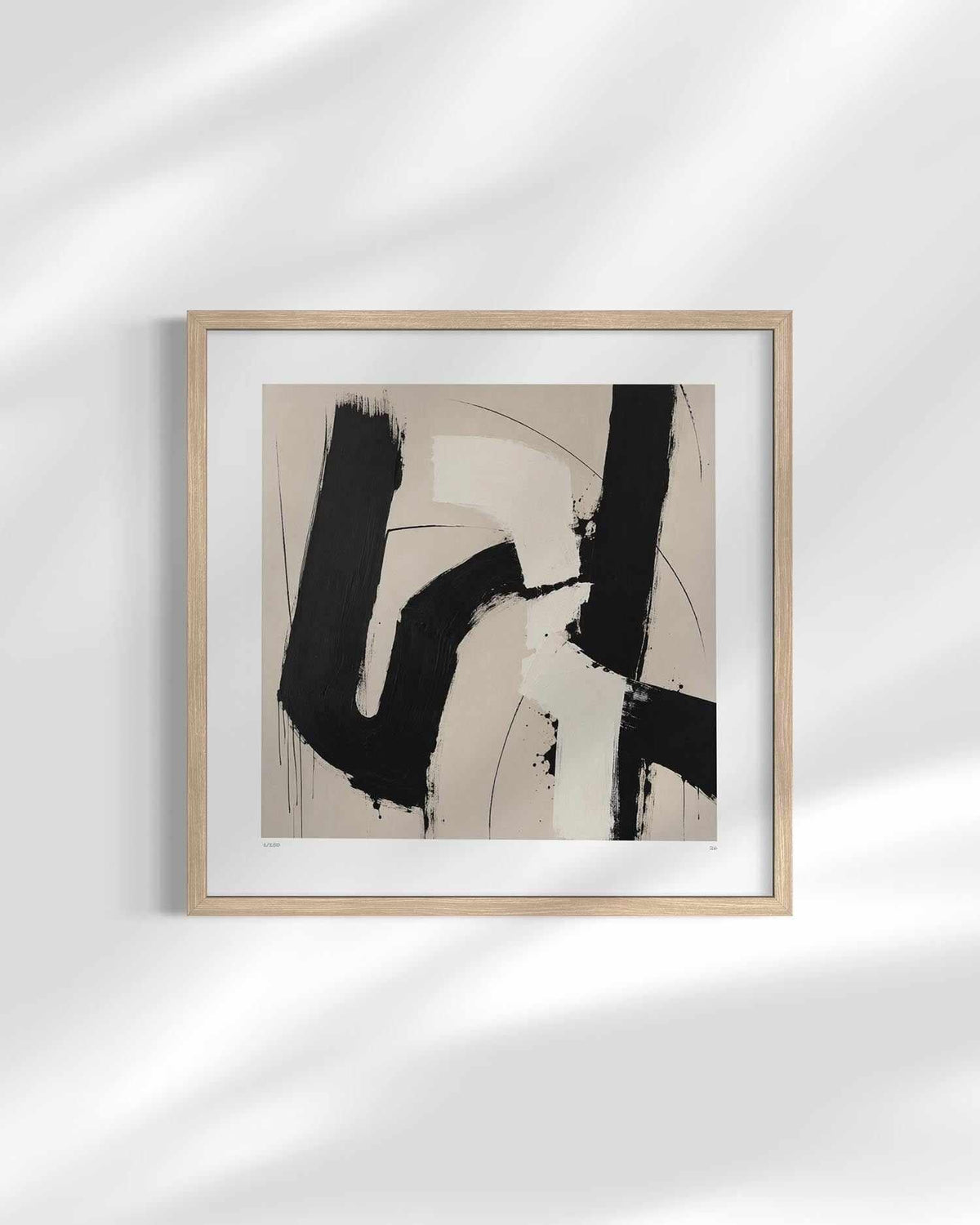 Framed abstract wall art featuring bold black brushstrokes on a warm beige background, displayed in a light wood frame with a white mat against a white wall with soft leaf shadows.