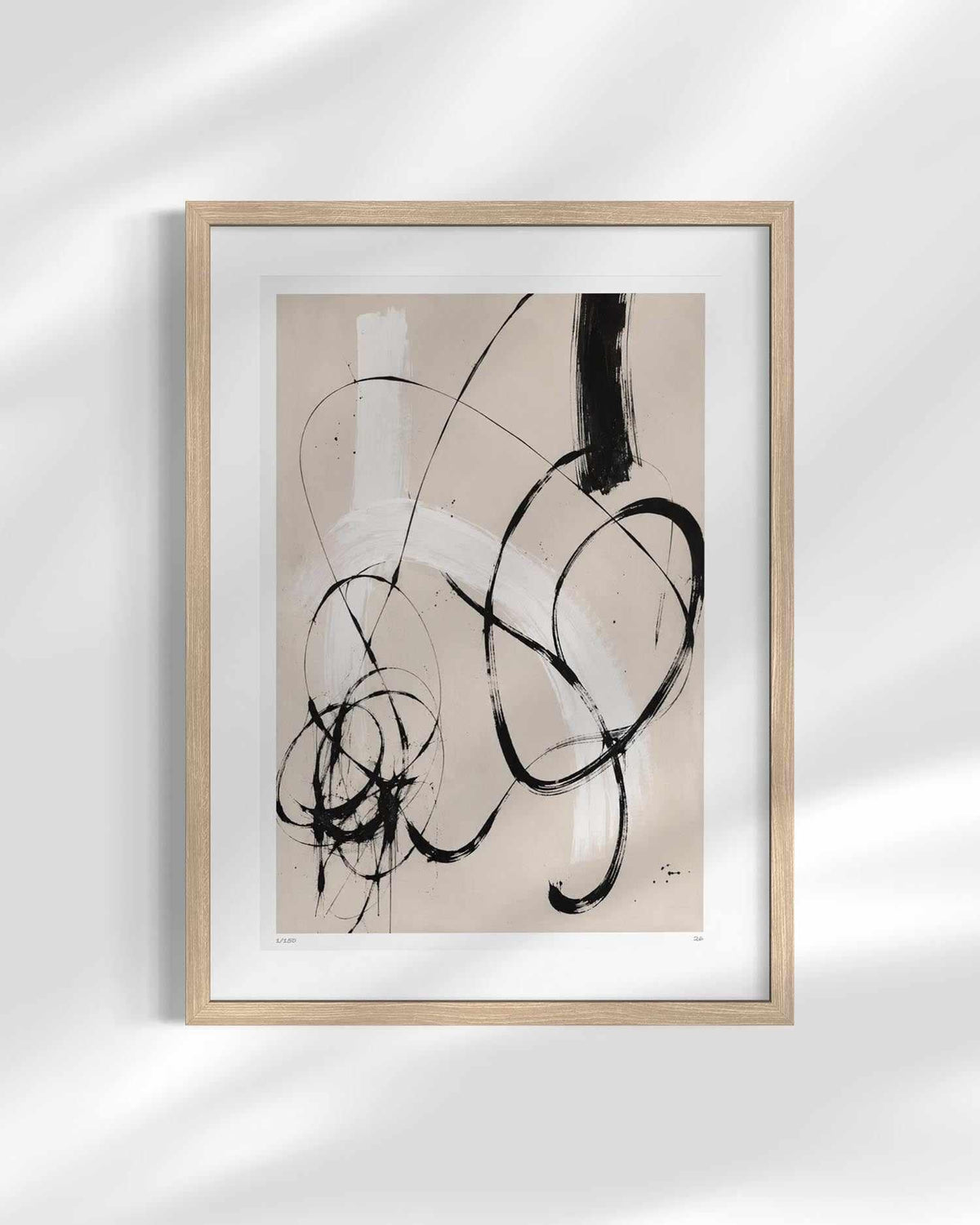 A framed abstract art print featuring black and white brushstrokes on a beige background, housed in a light wood frame with a white mat, displayed against a white wall with soft shadow overlays.