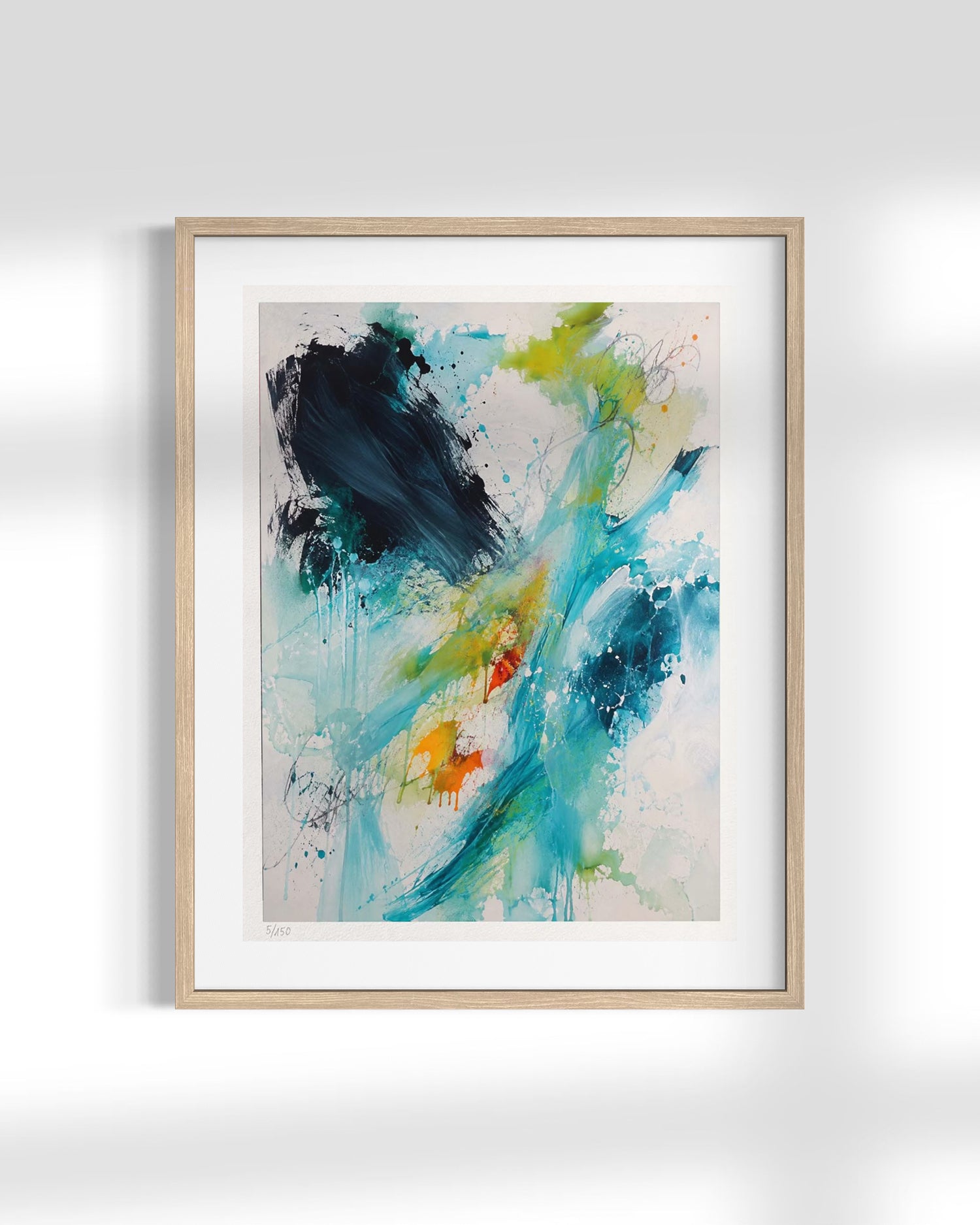 A framed abstract art print featuring expressive brushstrokes and splatters in teal, blue, green, black, and orange on a white mat, housed in a light natural wood frame against a white wall.