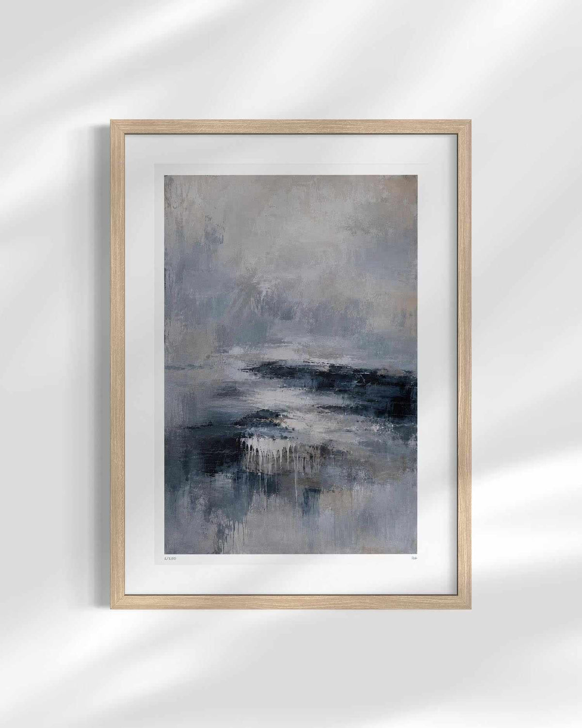 Framed abstract wall art print with a light wood frame and white mat, featuring soft gray, blue, and black brushstrokes, displayed against a white wall with soft shadow overlays.