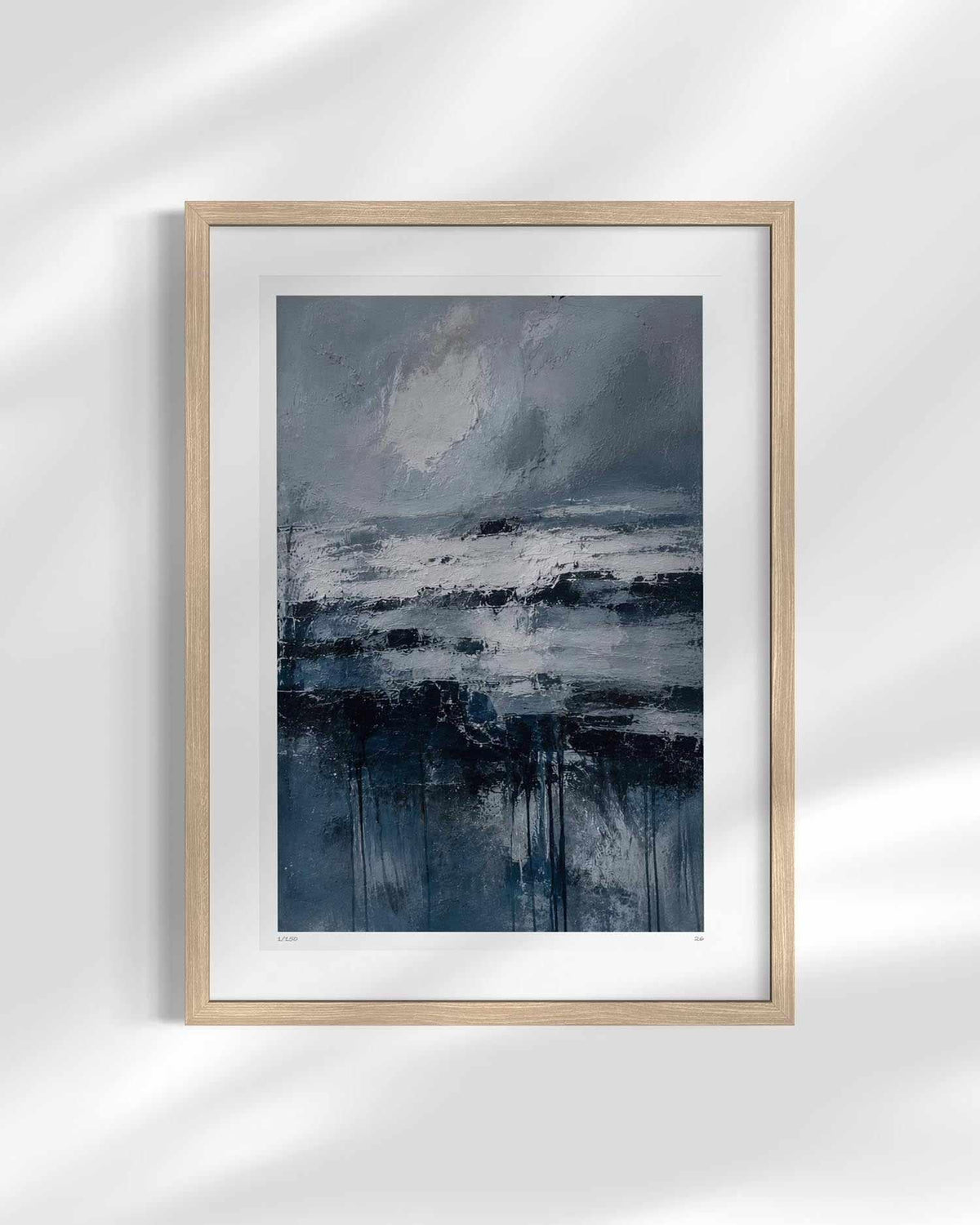 A framed abstract landscape painting featuring shades of blue, gray, and white, set in a light natural wood frame with a white mat, displayed against a white wall with soft shadow overlays.