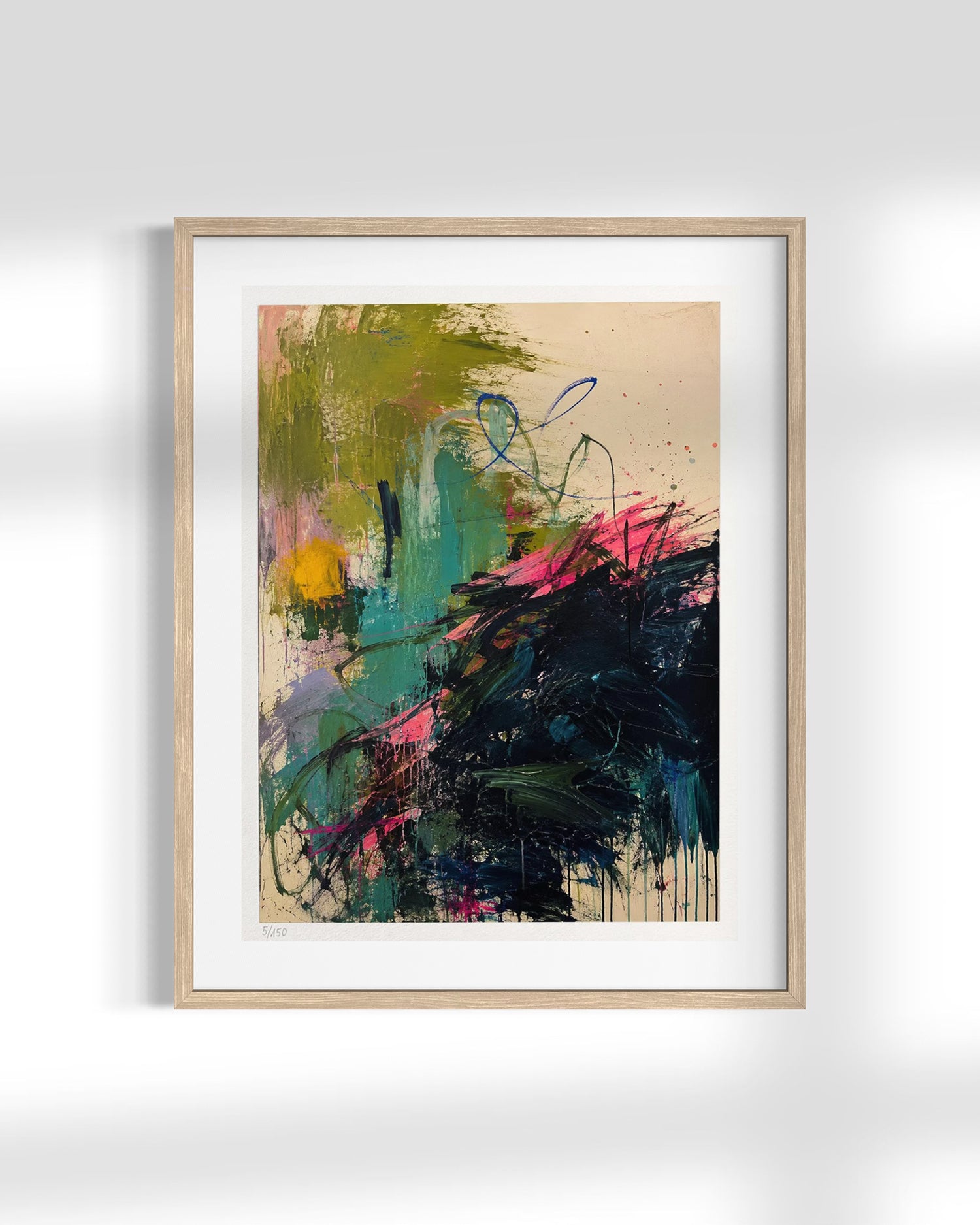 A framed abstract art print featuring expressive brushstrokes in green, teal, black, pink, and yellow on a beige background, housed in a light natural wood frame with a white mat, displayed against a light gray wall.
