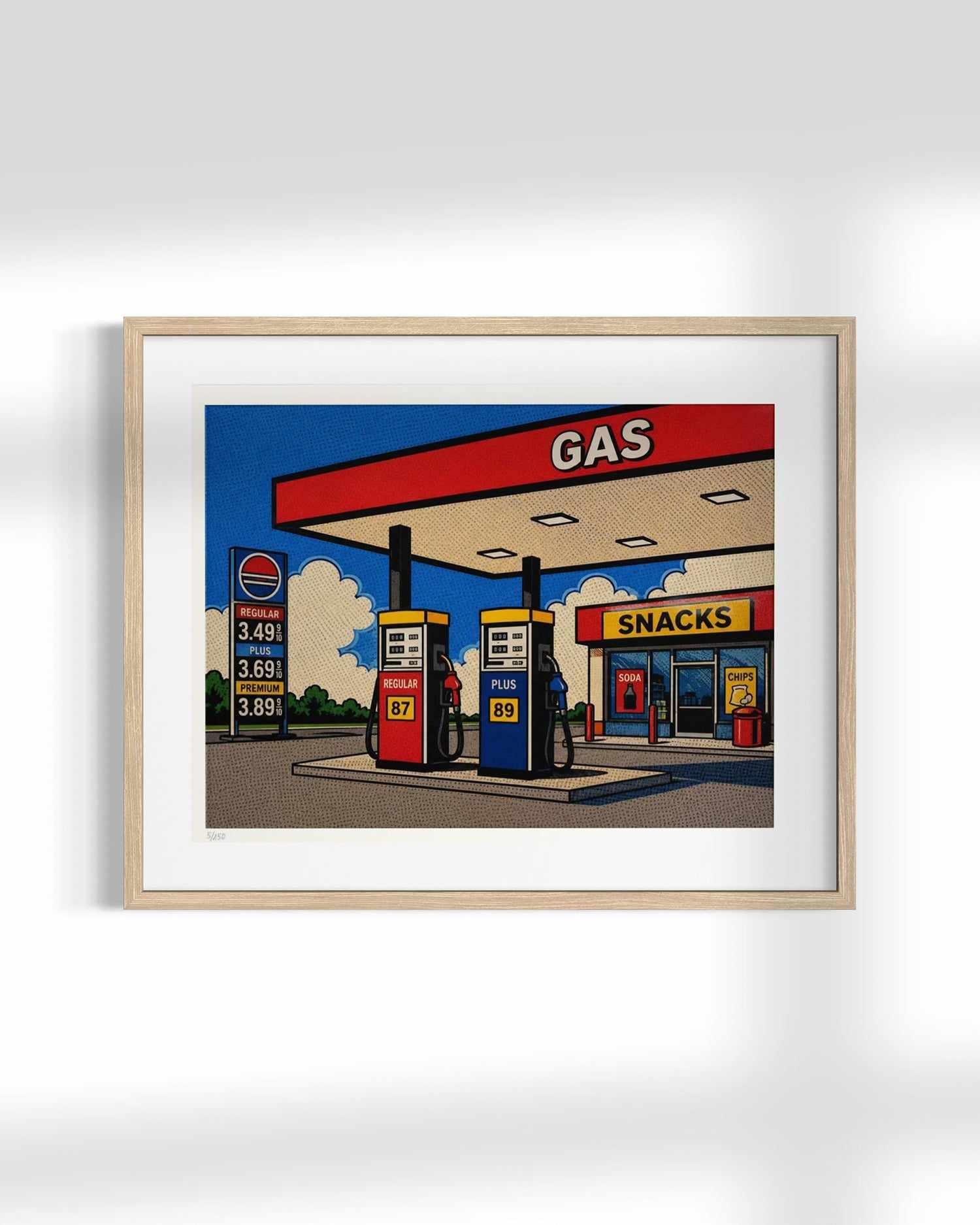 A framed pop-art style illustration of a gas station and convenience store, shown hanging on a light gray wall. The artwork features bold blue sky, red canopy signage, yellow snack shop signage, and colorful fuel pumps, enclosed in a light wood frame with a white mat.