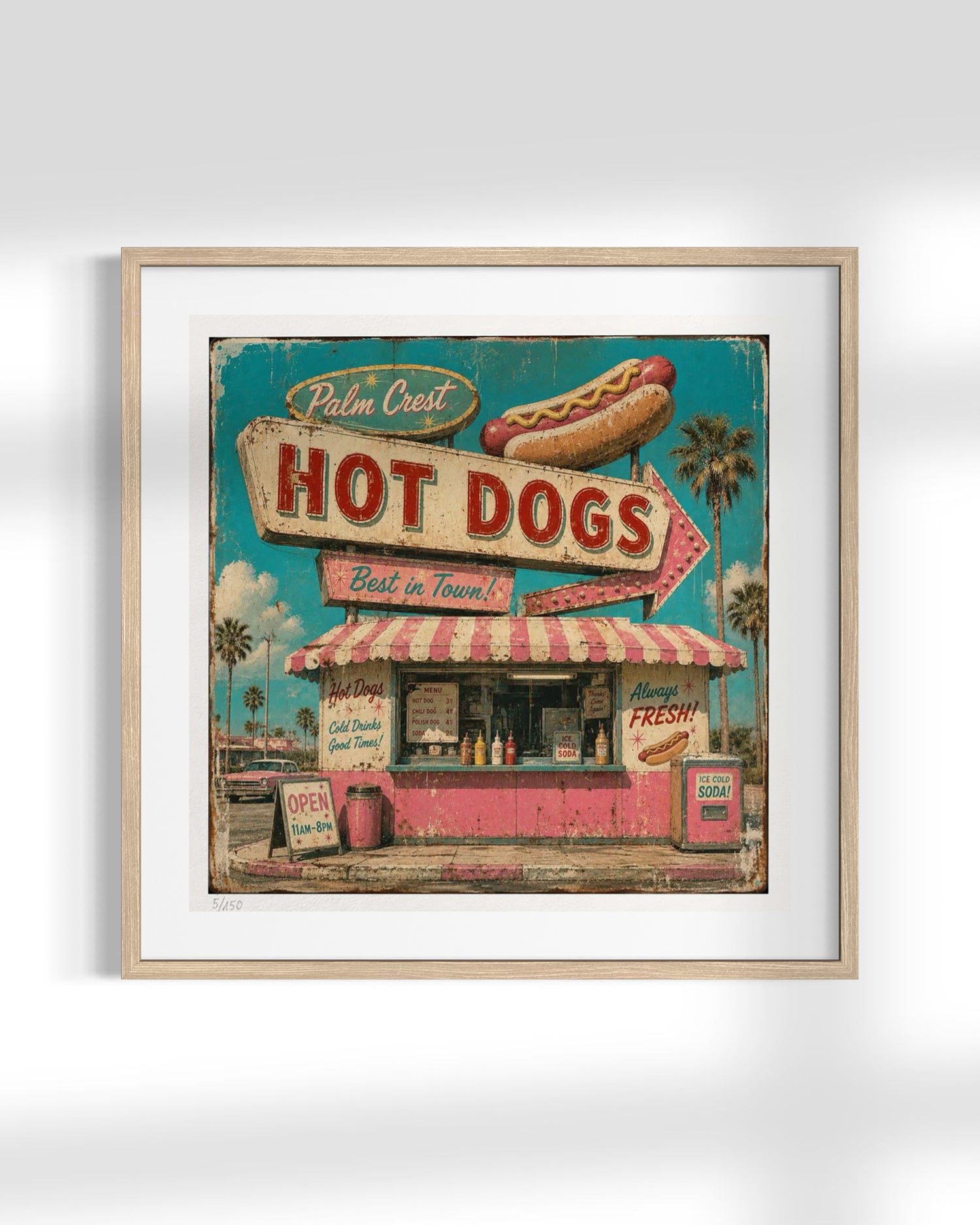 Framed vintage-style wall art featuring a retro hot dog stand sign with palm trees, a hot dog illustration, and distressed teal, pink, cream, and red tones, shown in a light wood frame against a white wall.