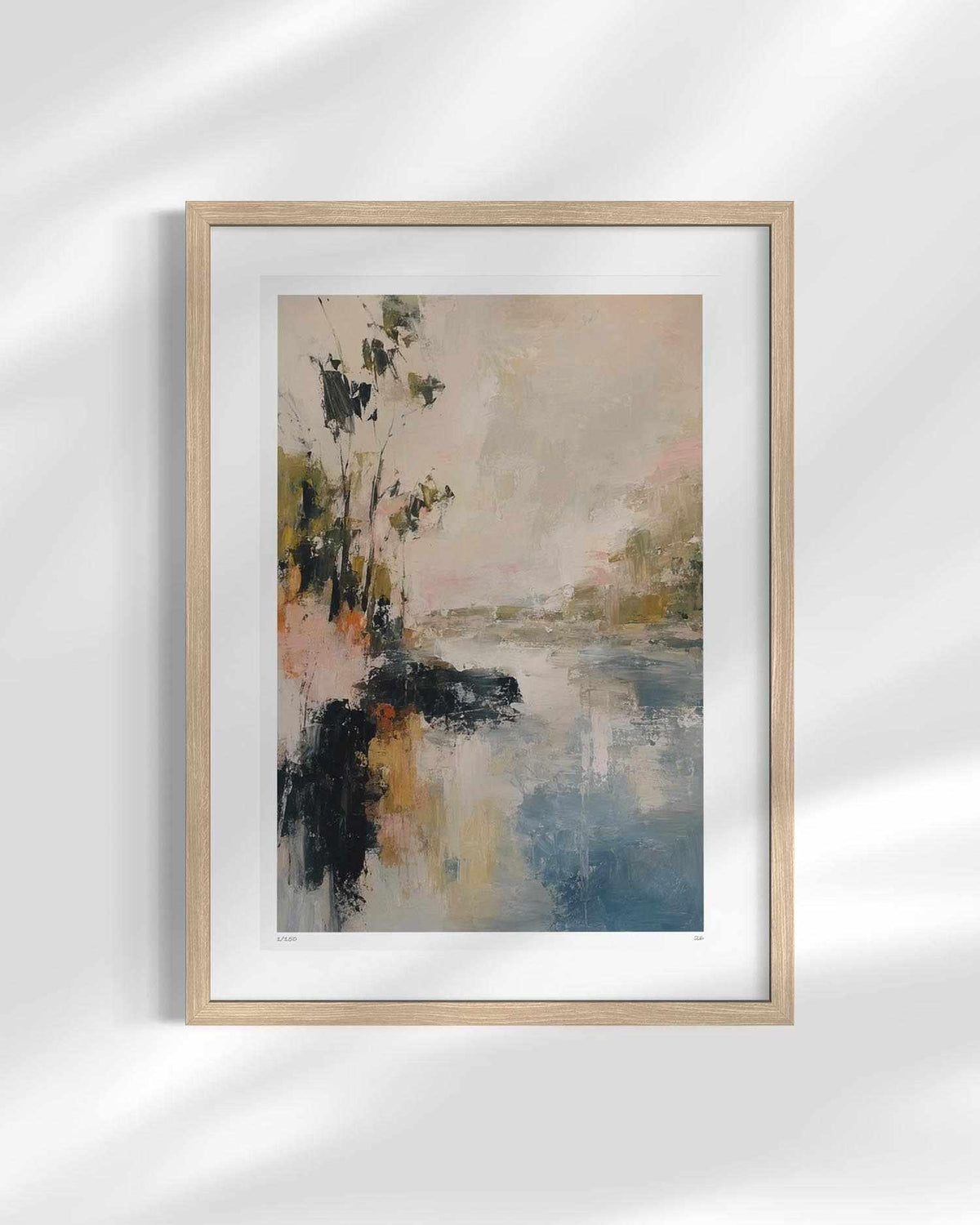 A framed abstract landscape art print featuring a river or lake scene with dark trees on the left, rendered in soft beige, blue, gray, and black tones. The print is matted and housed in a light natural wood frame, displayed against a white wall with soft diagonal shadows.