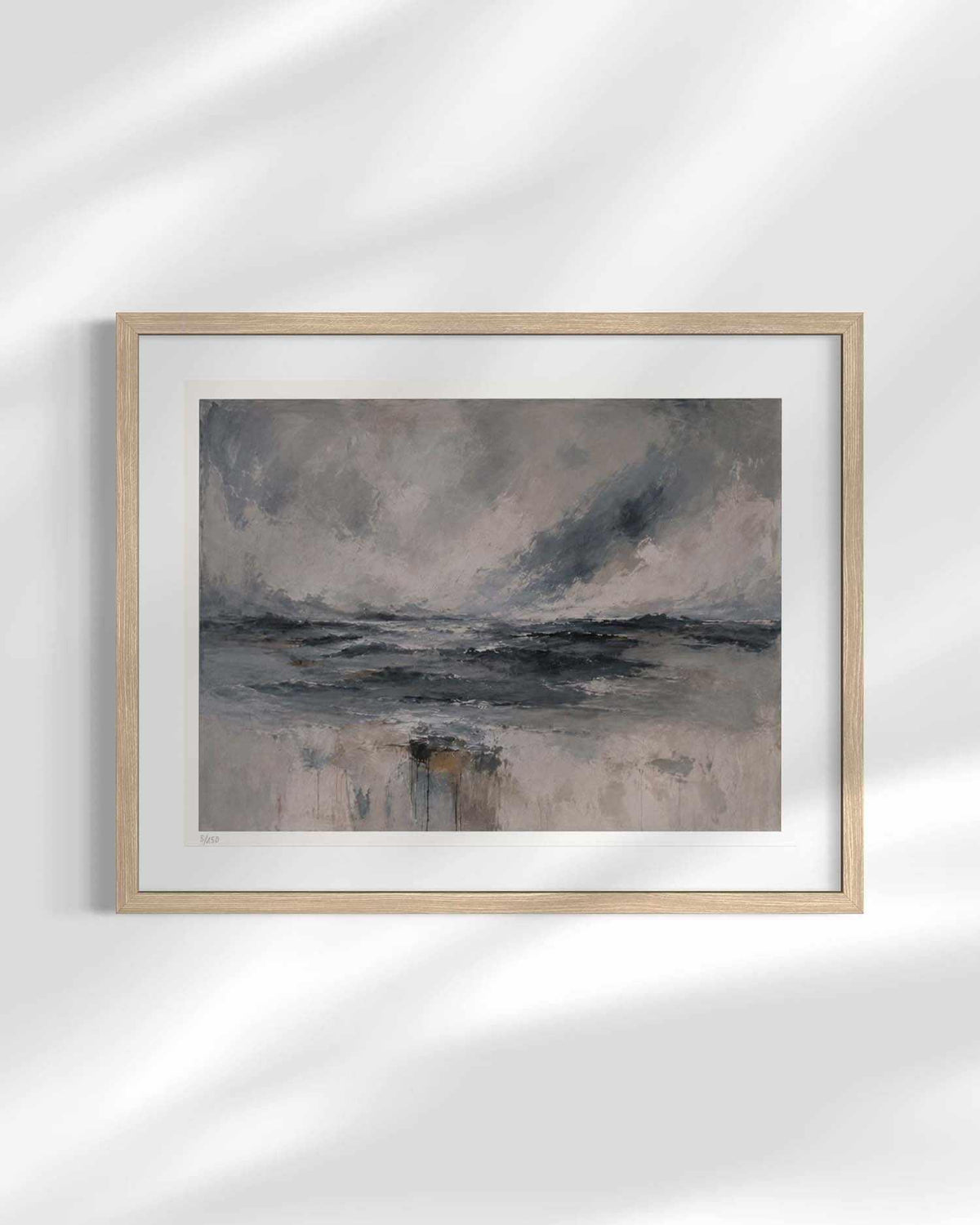 A framed abstract landscape painting featuring muted gray, blue, and beige tones, displayed on a white wall with soft diagonal shadows.