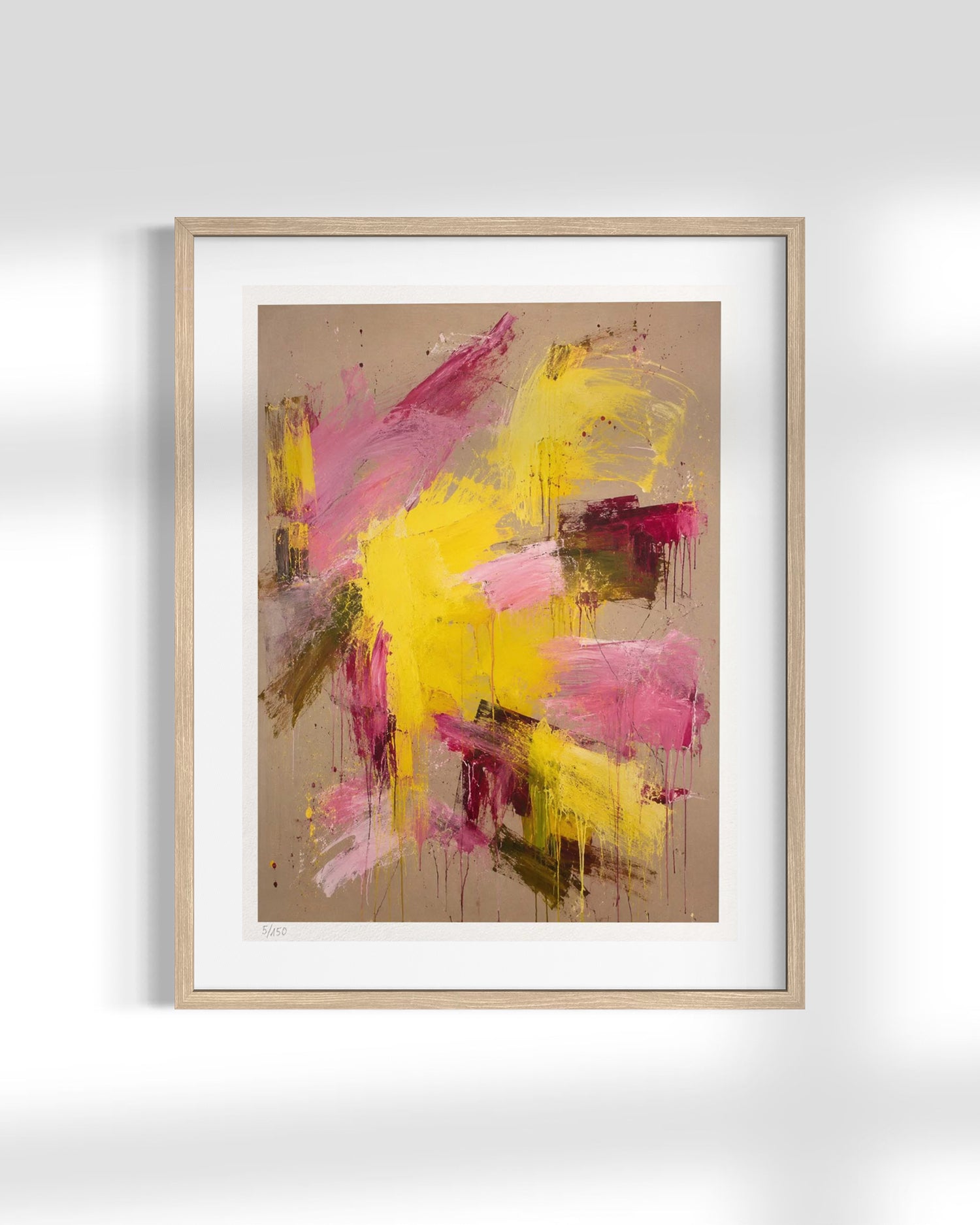Framed abstract wall art featuring expressive brushstrokes in yellow, pink, and magenta on a warm beige background, presented in a light wood frame with a white mat against a white wall.