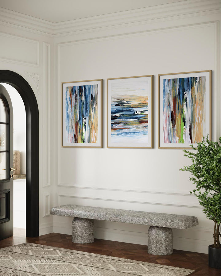 Three abstract paintings on a wall above a stone bench in a room with a plant and open door.