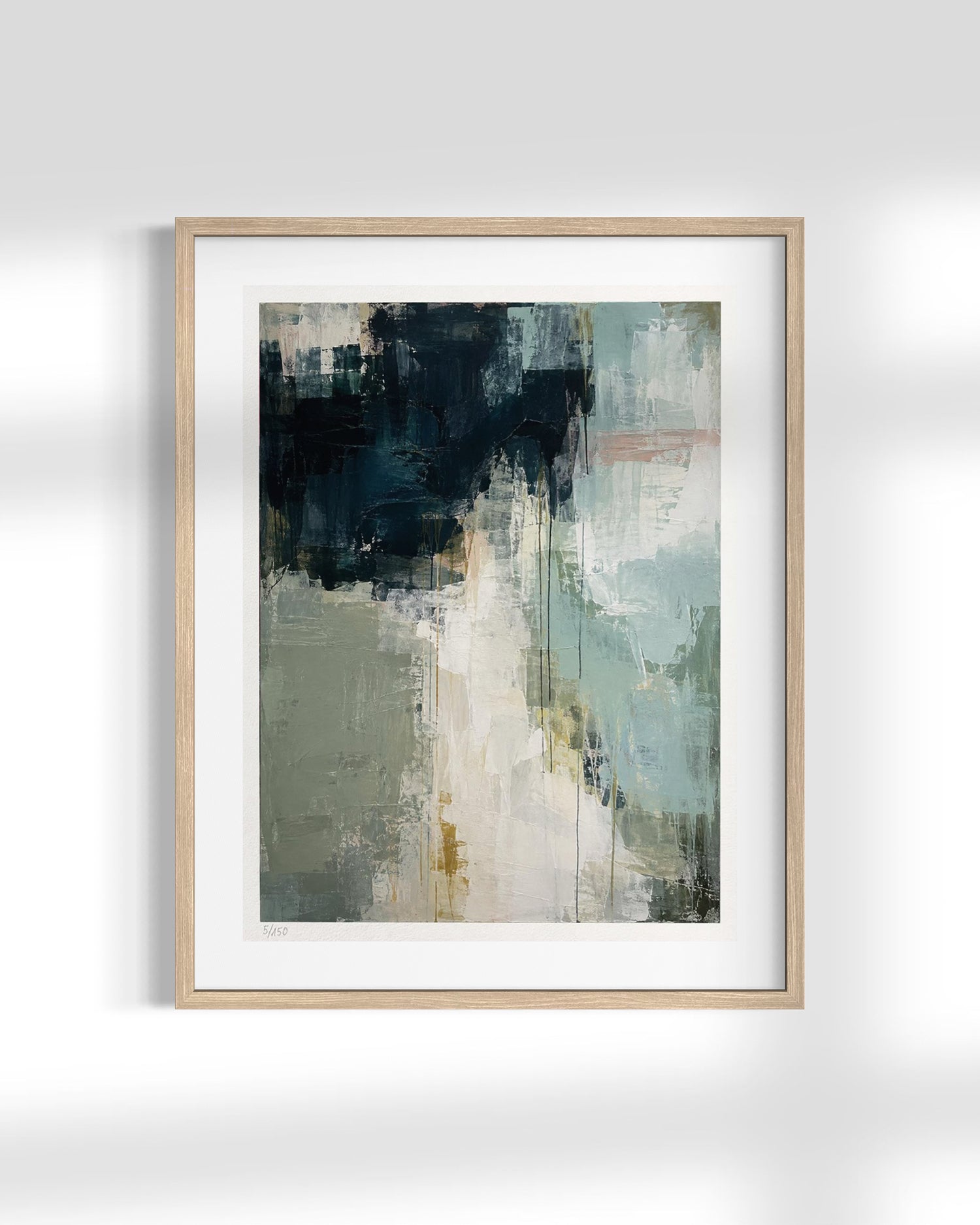 A framed abstract art print featuring a textured painting with dark navy, sage green, cream, and light blue brushstrokes, set in a light natural wood frame with a white mat against a white wall.