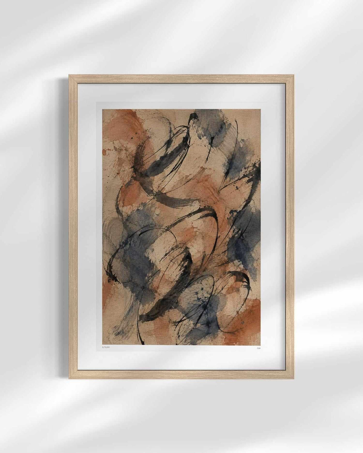 A framed abstract art print featuring expressive black, brown, and gray brushstrokes on a warm beige background, housed in a light natural wood frame with a white mat, displayed against a white wall with soft shadow overlays.
