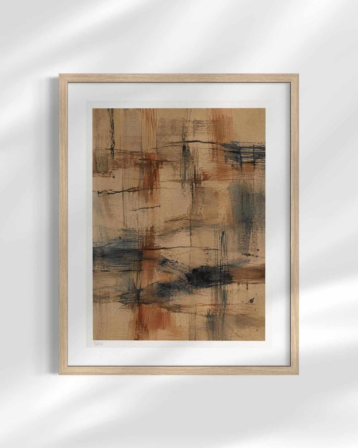 Framed abstract art print featuring a textured composition of beige, brown, and charcoal gray brushstrokes, presented in a light natural wood frame with a white mat against a white wall with soft shadow overlays.