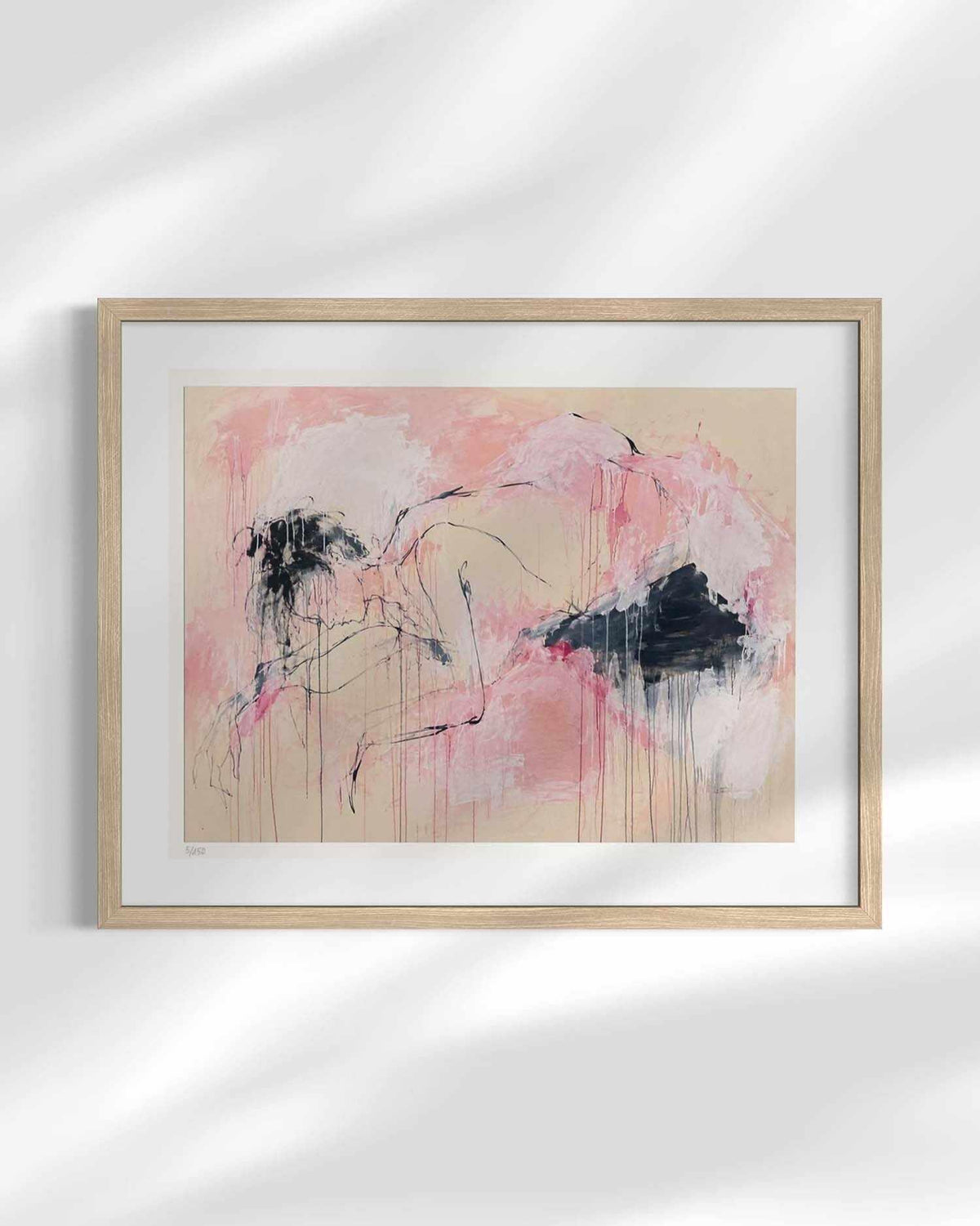 Framed abstract art print featuring pink, beige, and black brushstrokes, displayed in a light wood frame with a white mat against a white wall with soft shadow overlays.