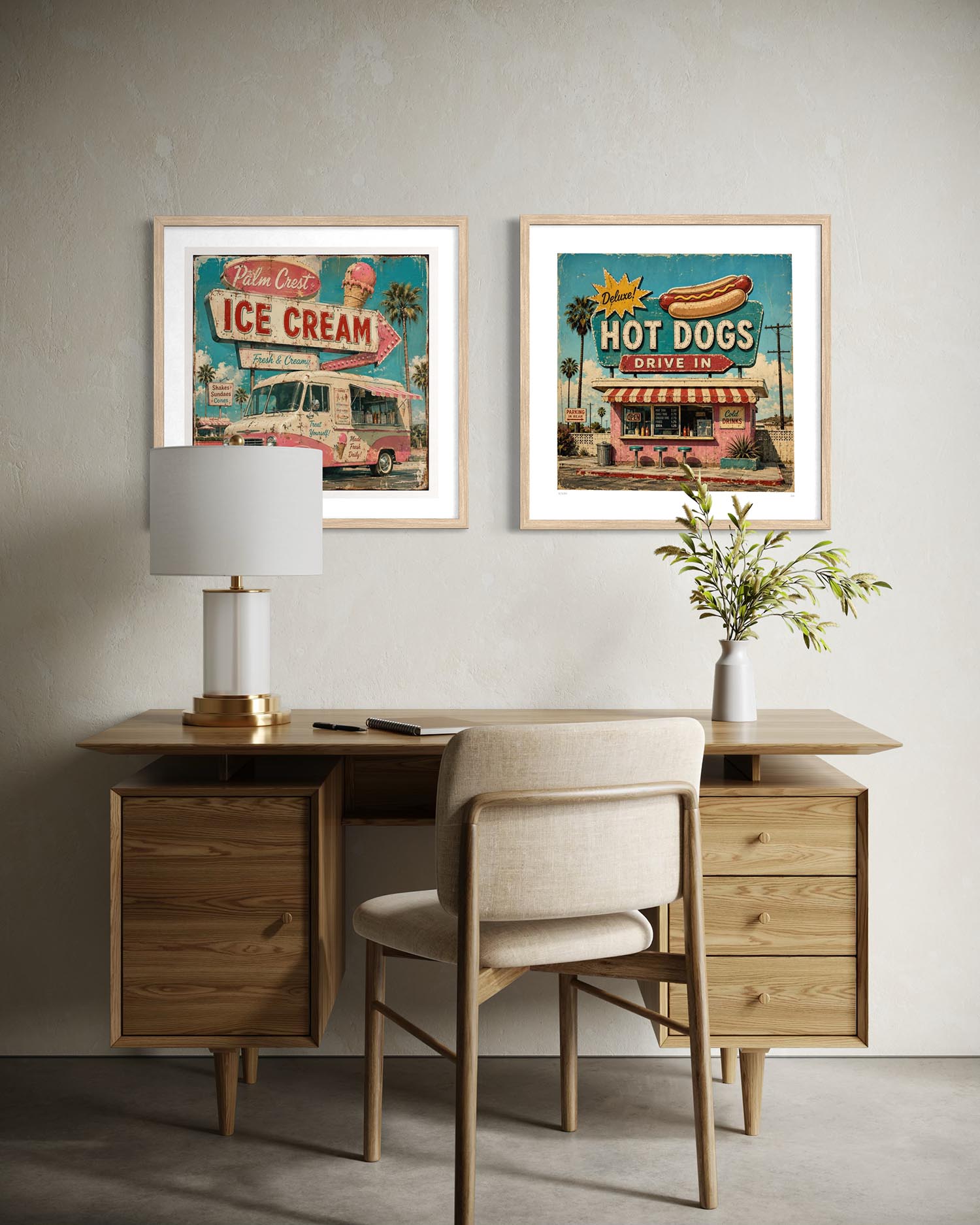 Two framed retro-style art prints hang on a textured light gray wall above a wooden desk with a chair, lamp, and vase in a styled interior setting.
