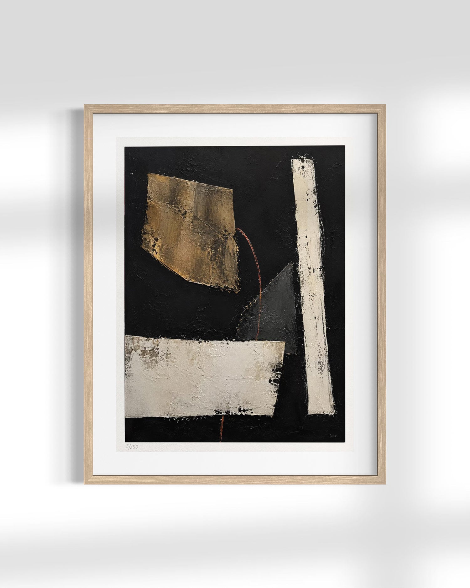 A framed abstract art print featuring a black background with textured white and gold geometric shapes, presented in a light oak frame with a white mat against a light gray wall.